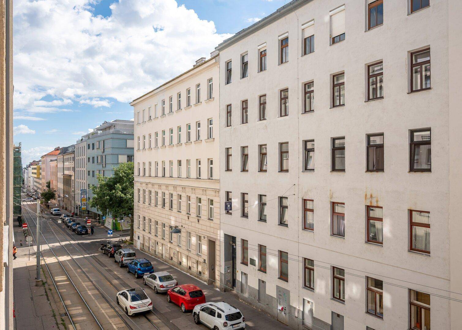 Weitläufiger Blick auf die Stadtstraße mit parkenden Autos und Wohngebäuden unter blauem Himmel.
