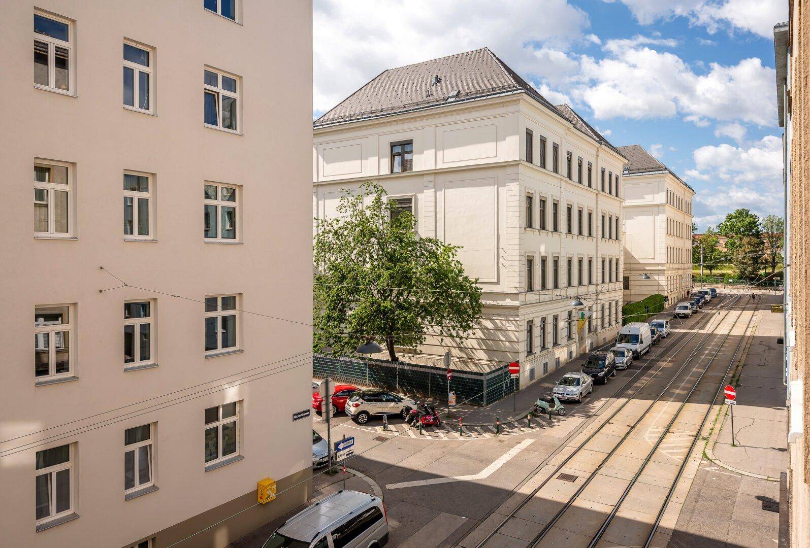 Blick auf die belebte Straße mit historischen Gebäuden und Straßenbahnschienen unter blauem Himmel.