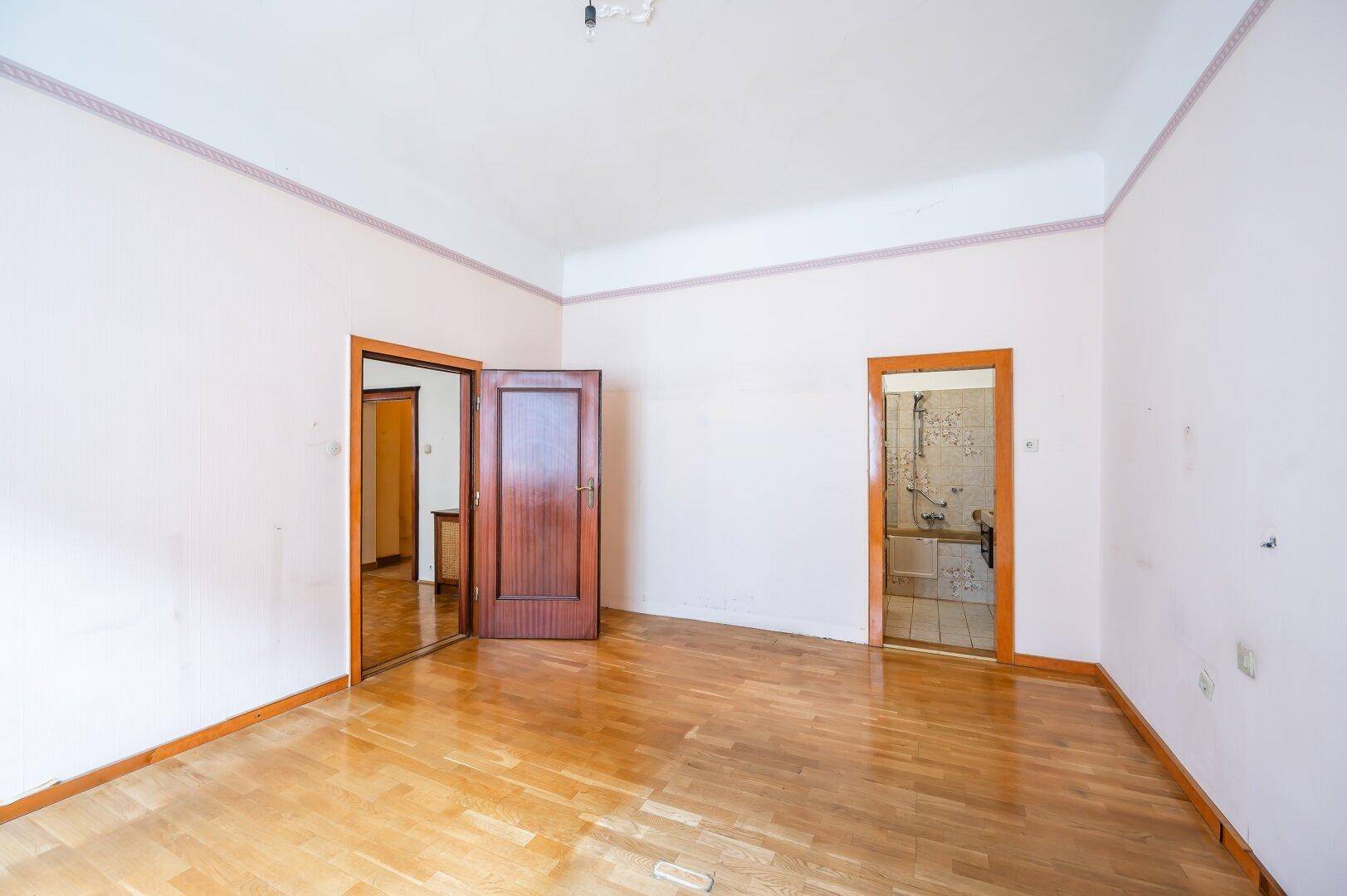 Geräumiges Zimmer mit Holzboden und Zugang zu weiteren Räumen, ideal für Renovierungsprojekte.