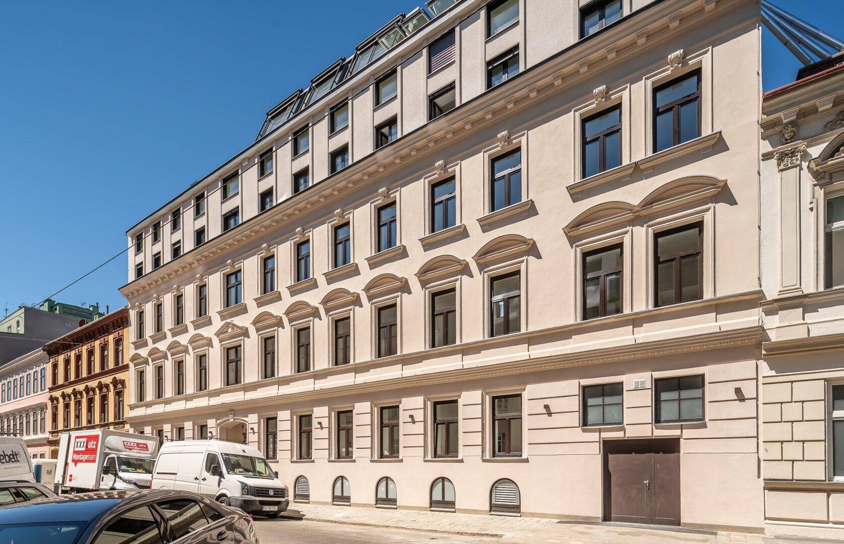 Klassische Fassade eines Mehrfamilienhauses mit vielen Fenstern und architektonischen Details an einer Stadtstraße.