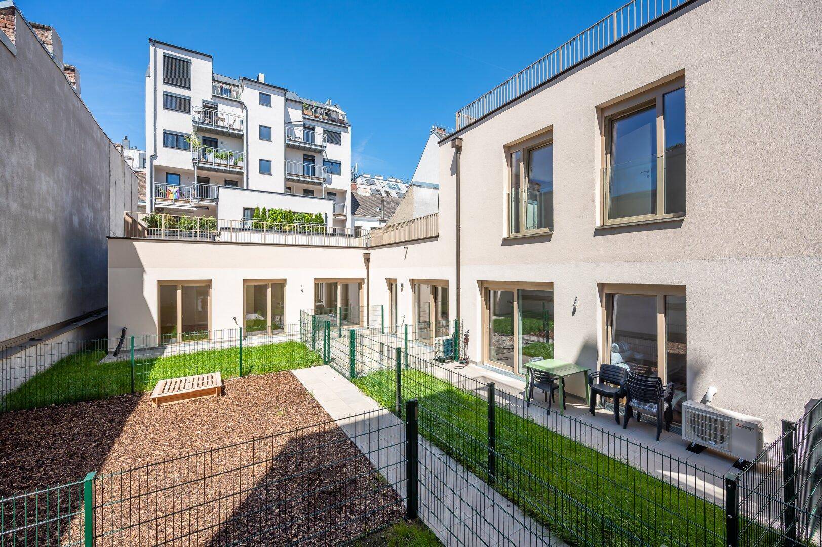 Innenhof mit kleinen Gartenflächen, Sitzgelegenheiten und Blick auf umliegende Gebäude.