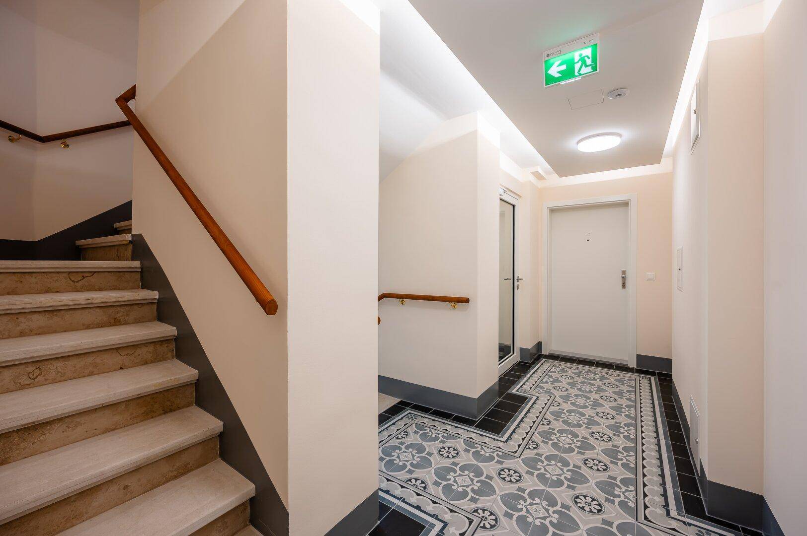 Eingangsbereich mit gemusterten Fliesen, Treppe und Zugang zu den Wohnungen.