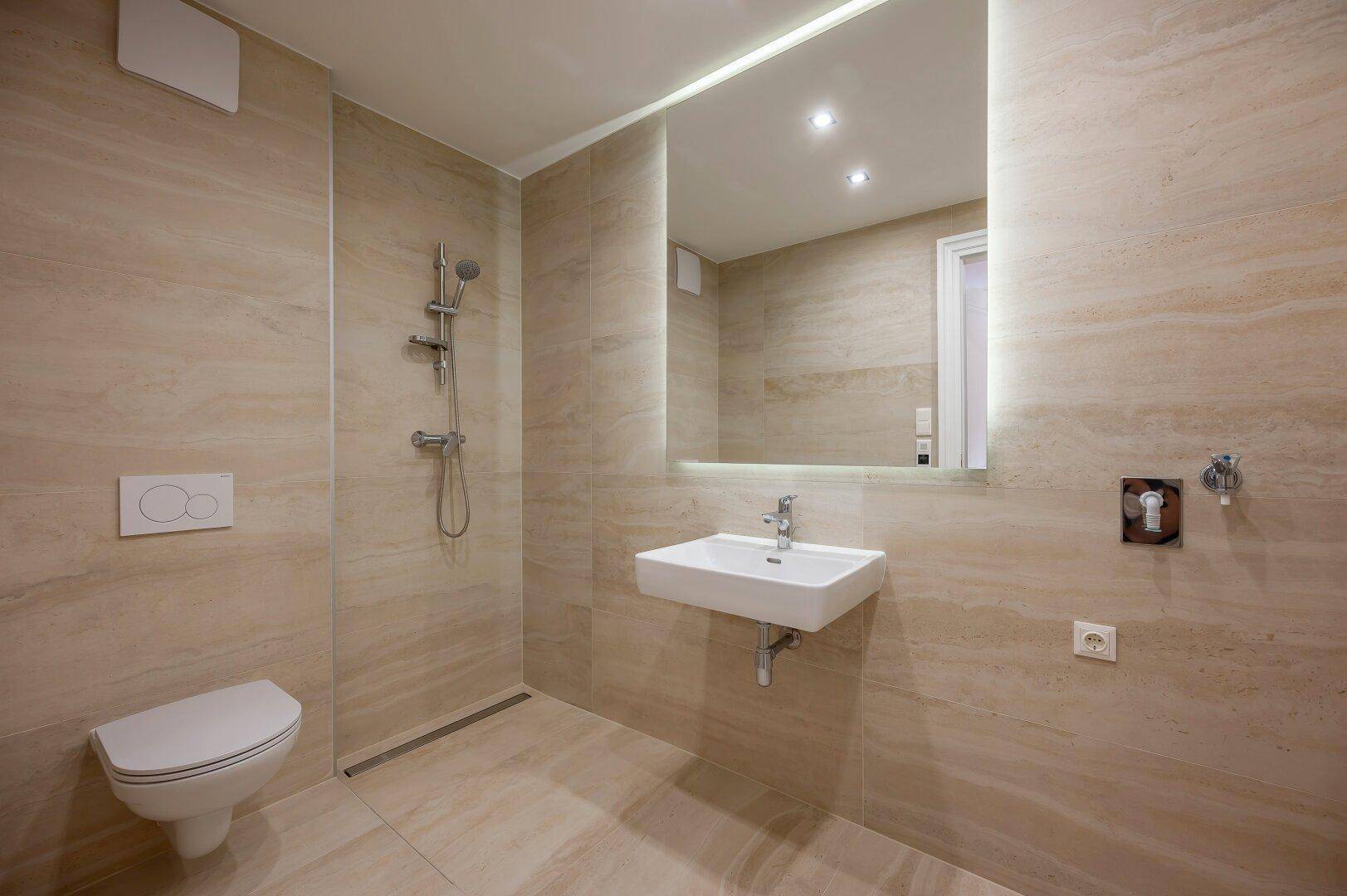 Modernes Badezimmer mit beigen Fliesen, wandhängendem WC, Waschbecken und ebenerdiger Dusche.
