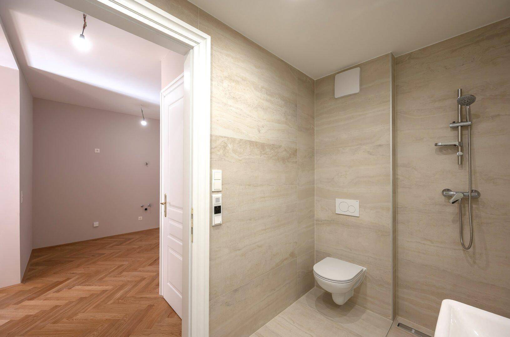 Modernes Badezimmer mit beigen Fliesen und ebenerdiger Dusche, angrenzend an einen hellen Raum.