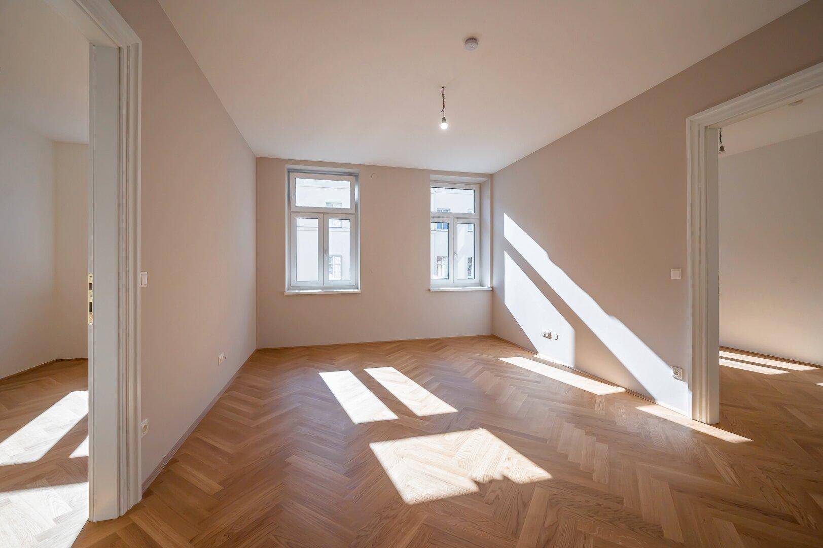 Geräumiges Wohnzimmer mit Fischgrätparkett und viel natürlichem Licht, bereit zur individuellen Gestaltung.