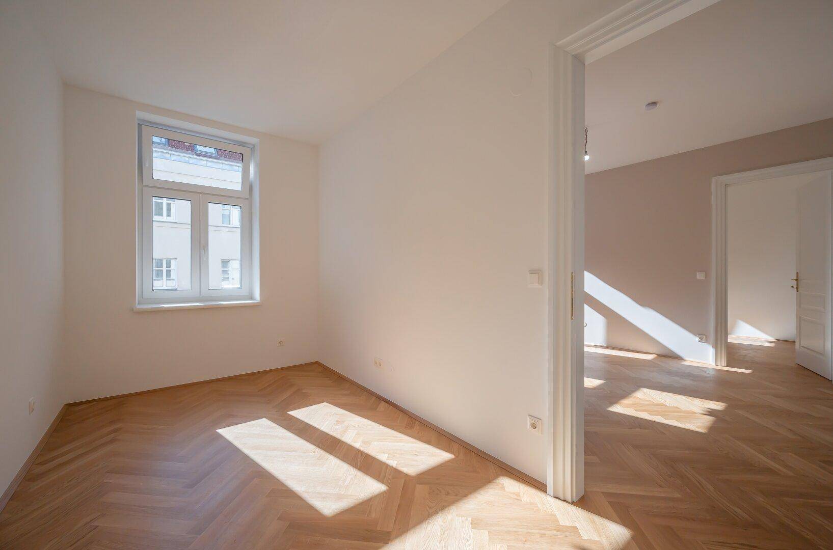 Helles Schlafzimmer mit Fischgrätparkett und großem Fenster, ideal für ruhige Stunden.