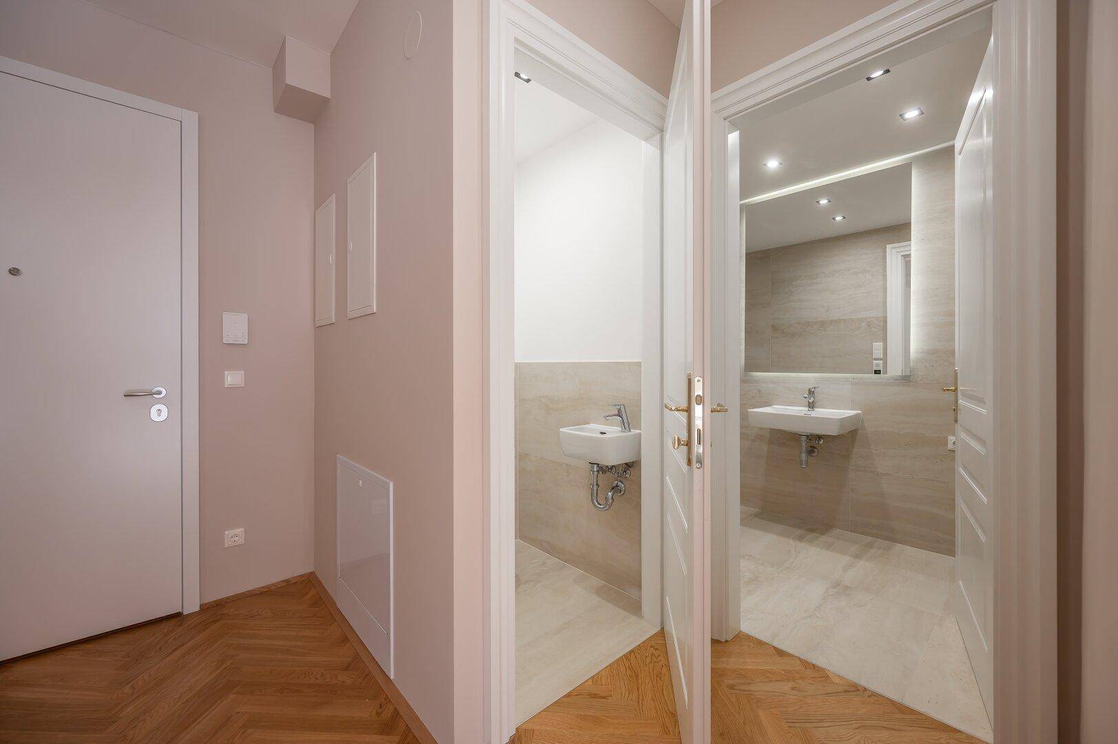 Heller Eingangsbereich mit Fischgrätparkett und Blick in das moderne Badezimmer und Gäste-WC.