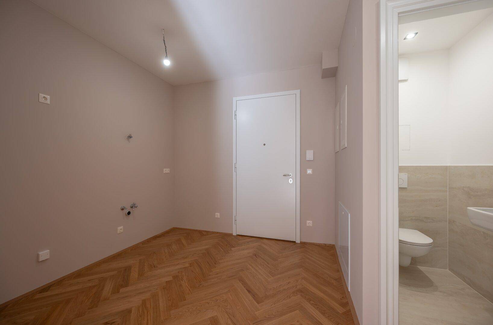 Eingangsbereich mit Fischgrätparkett und Blick auf die Eingangstür und das angrenzende Badezimmer.