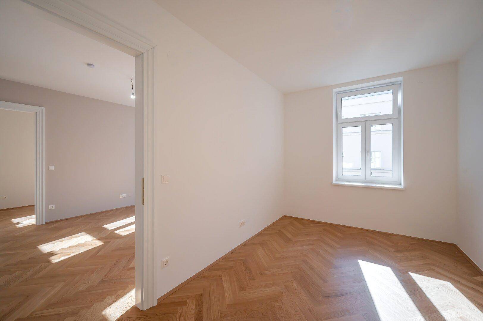 Gemütliches Zimmer mit hellem Fischgrätparkett und weiß gestrichenen Wänden, ideal als Schlafzimmer.