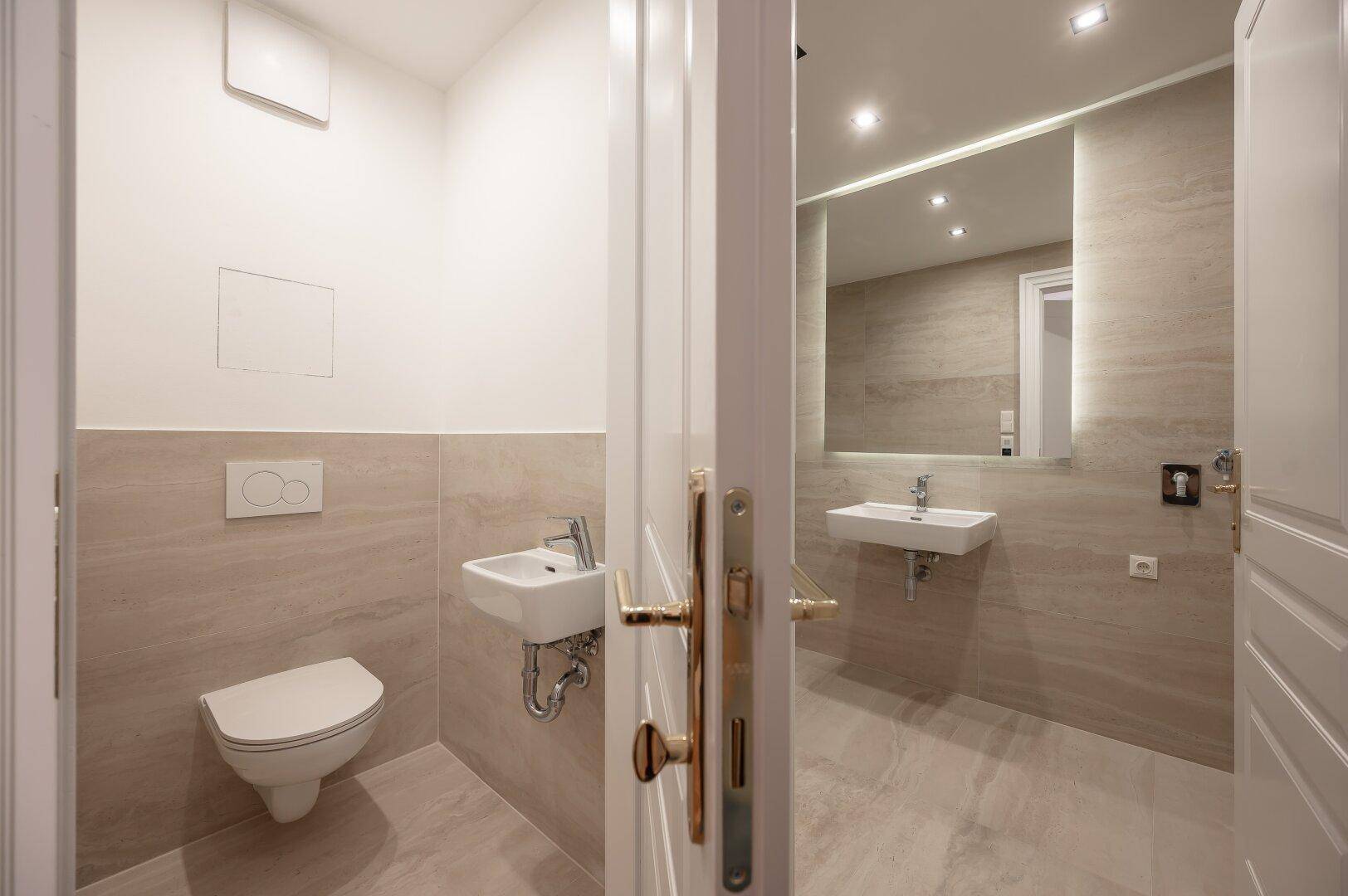 Modernes Gäste-WC mit Wand-WC, kleinem Waschbecken und hellen, großformatigen Fliesen.