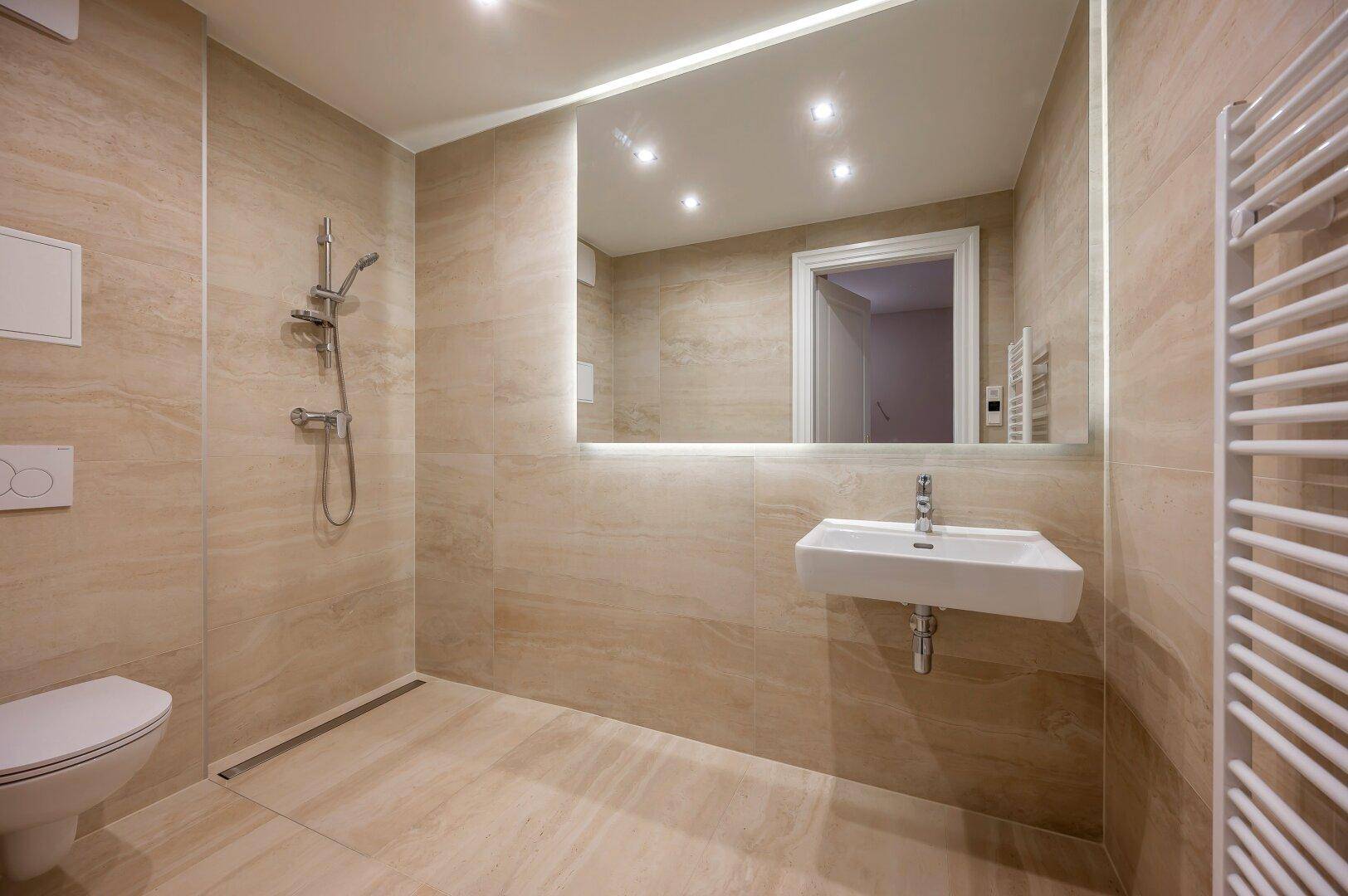 Modernes Badezimmer mit beigefarbenen Fliesen, ebenerdiger Dusche, Wand-WC und beheiztem Handtuchhalter.