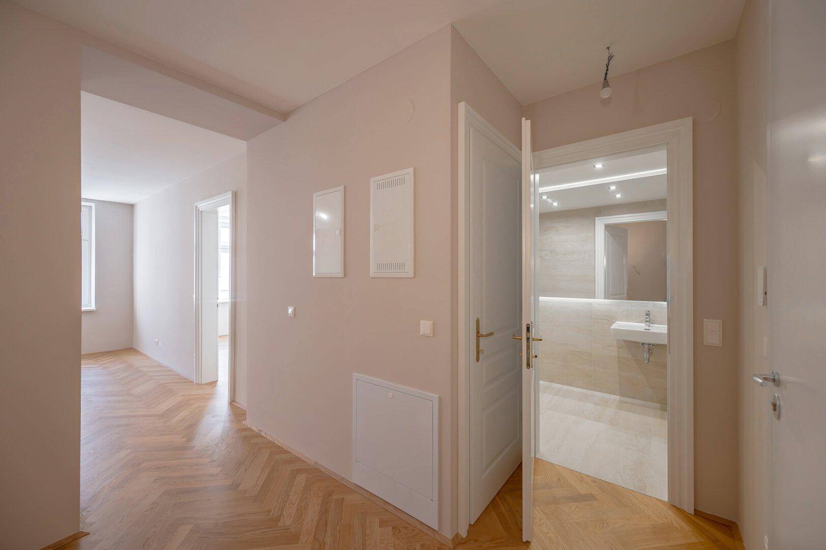 Heller Flur mit Fischgrätparkett und Blick in ein modernes Badezimmer, frisch renoviert.