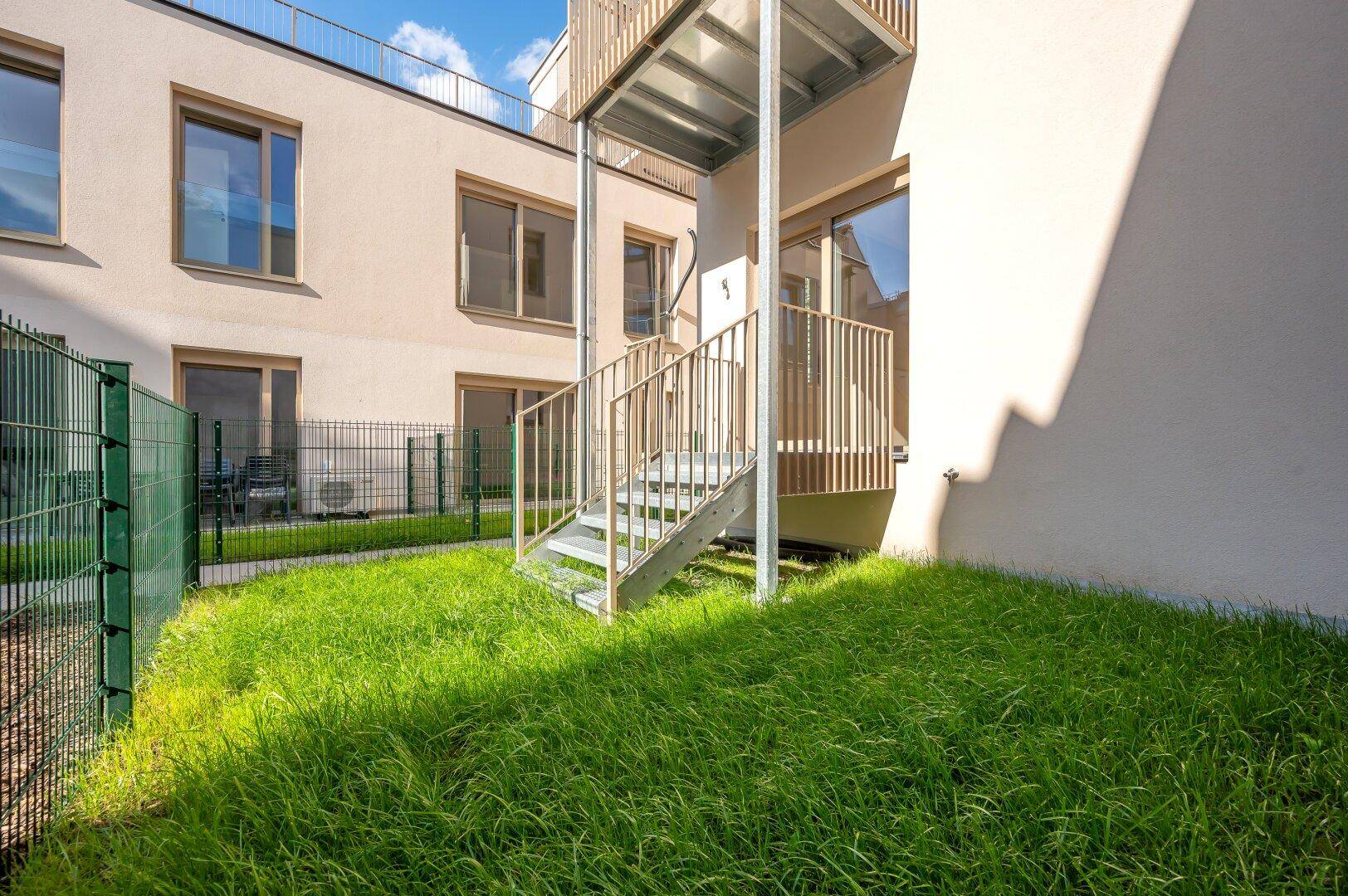 Kleiner Gartenbereich mit frischem Rasen und einer Außentreppe, die zu einem oberen Balkon führt.