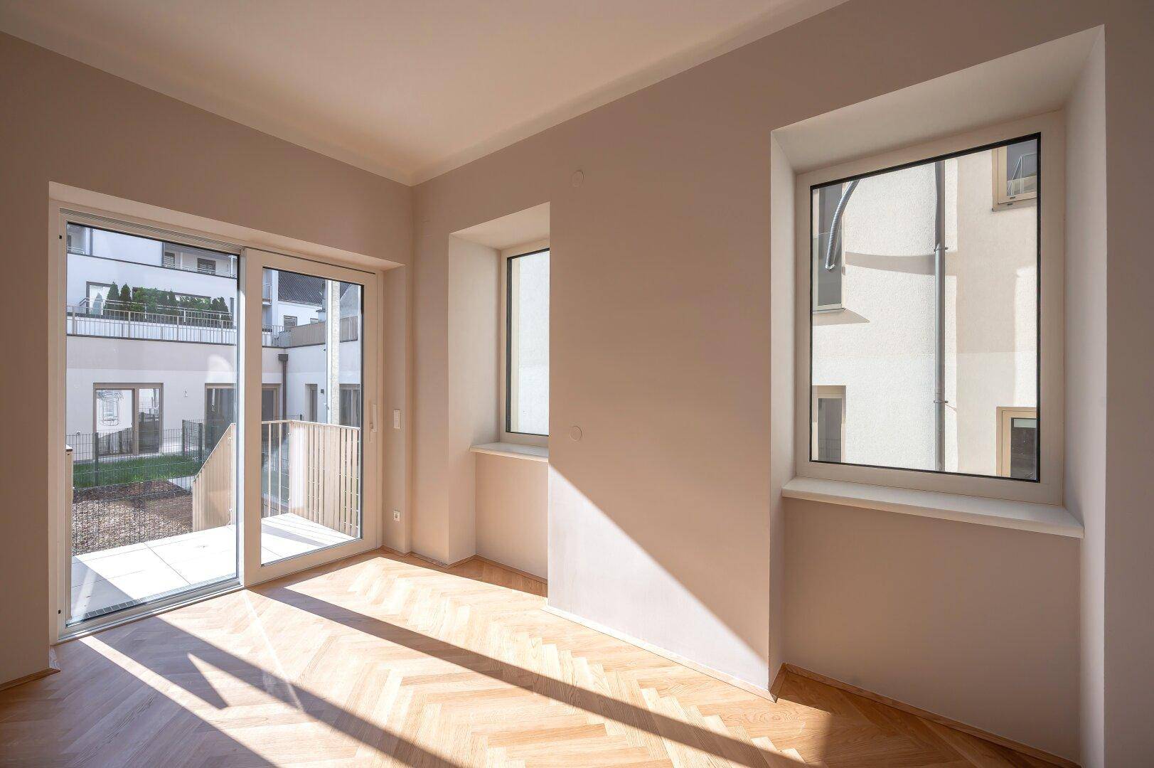 Geräumiges Zimmer mit Fischgrätparkett, viel Tageslicht und direktem Zugang zum Balkon.