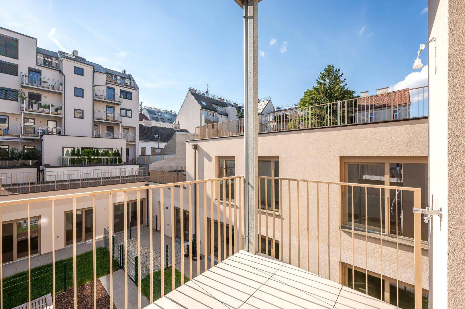 Sonniger Balkon mit Blick auf einen begrünten Innenhof und die moderne Wohnanlage.