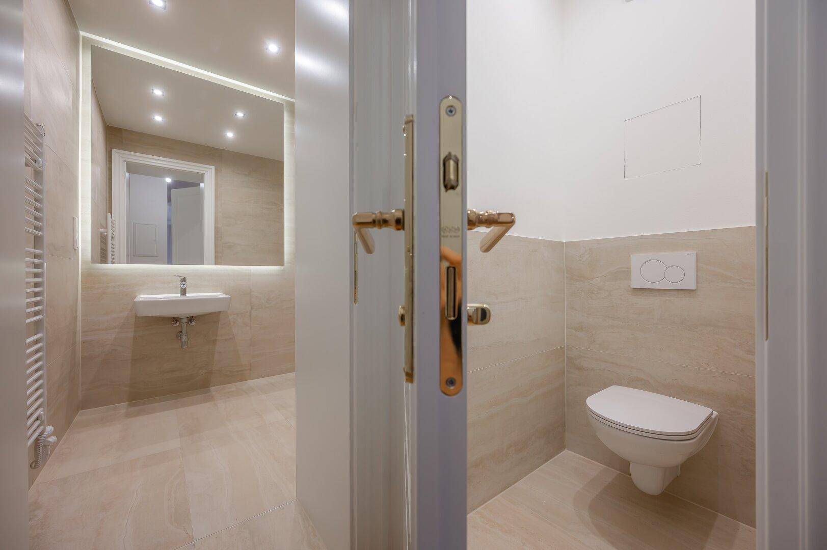 Modernes WC mit wandhängender Toilette und beigefarbenen Fliesen, angrenzend an das Badezimmer.
