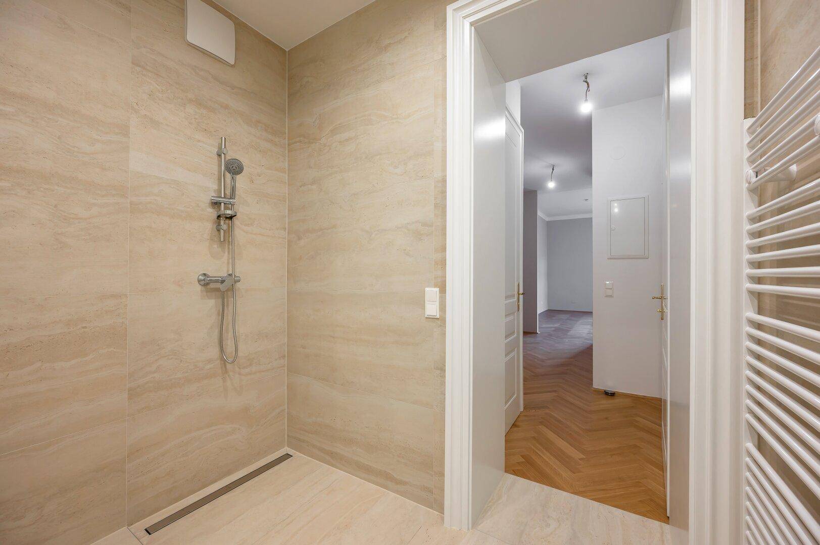 Elegantes Badezimmer mit beigefarbenen Fliesen, geräumiger Dusche und Handtuchheizkörper.