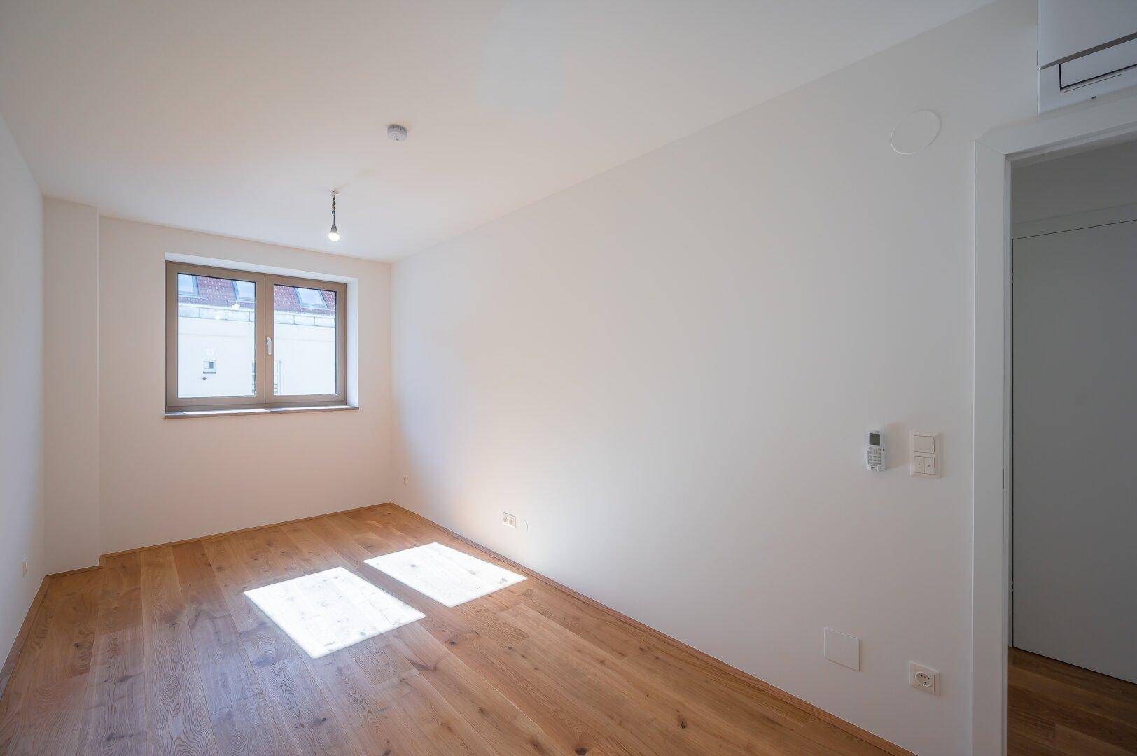 Helles Schlafzimmer mit Holzboden und einem Fenster, das viel Tageslicht hereinlässt.