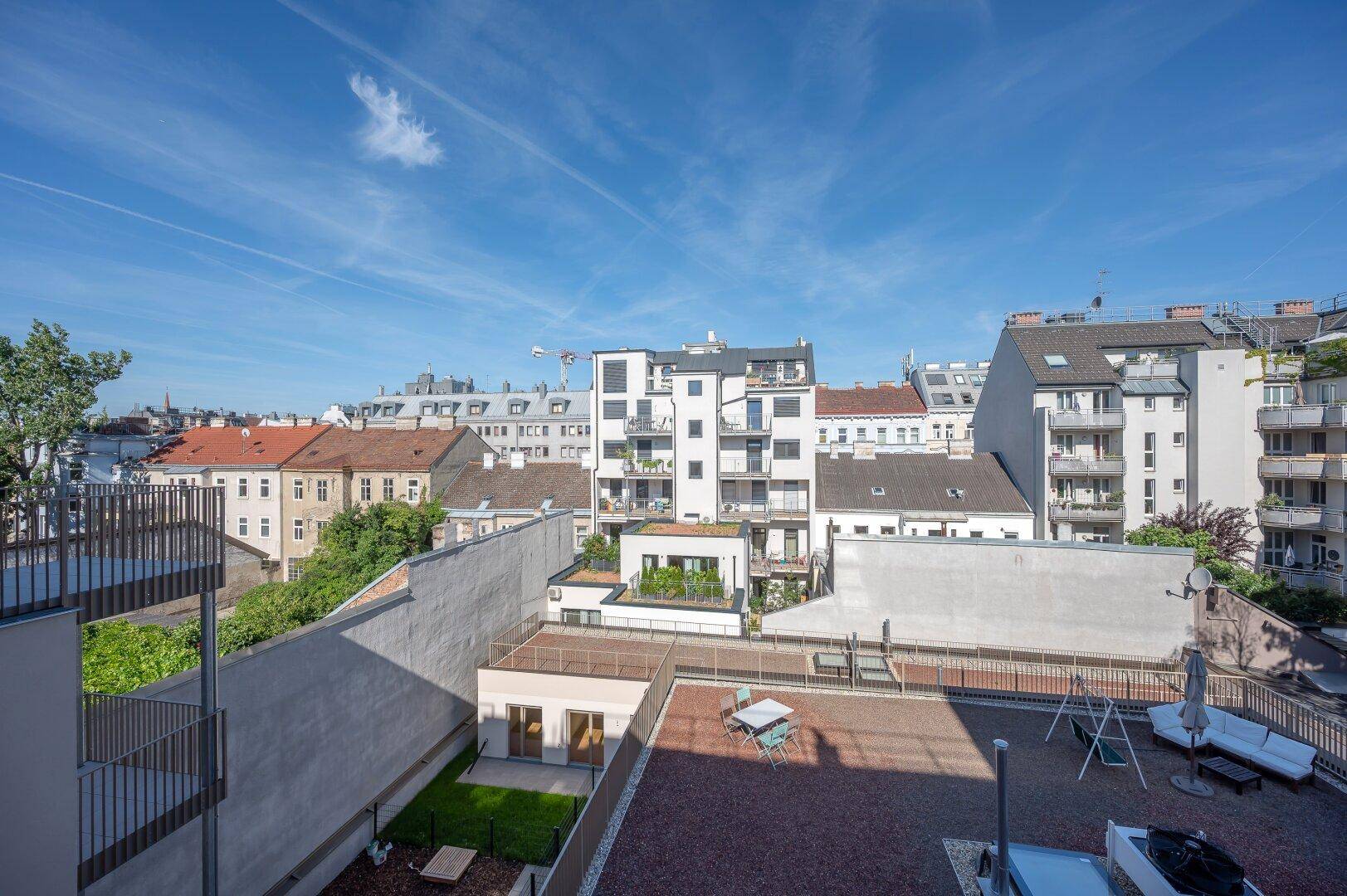 Dachterrasse mit Grünflächen, Sitzgelegenheiten und Blick auf die Stadt.