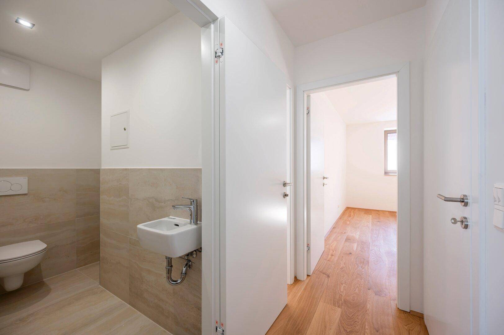 Separates Gäste-WC mit kleinem Waschbecken und Wand-WC, modern gefliest.