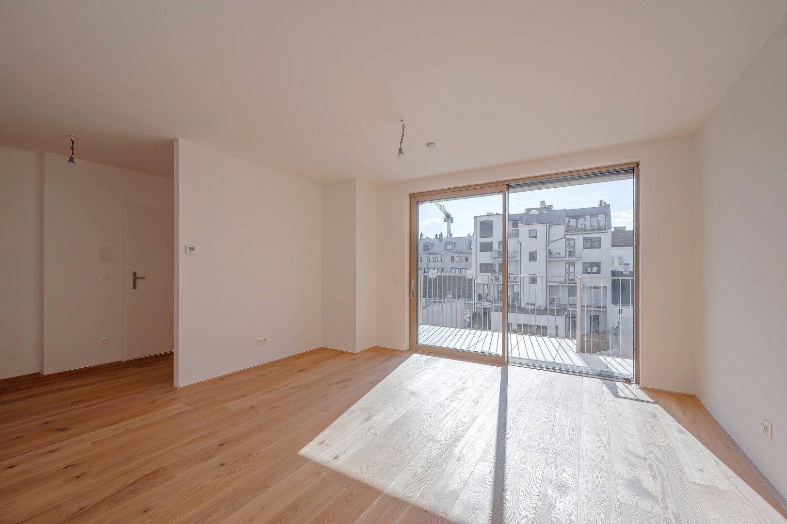 Lichtdurchfluteter Wohnbereich mit Holzboden und großen Schiebetüren zum Balkon.