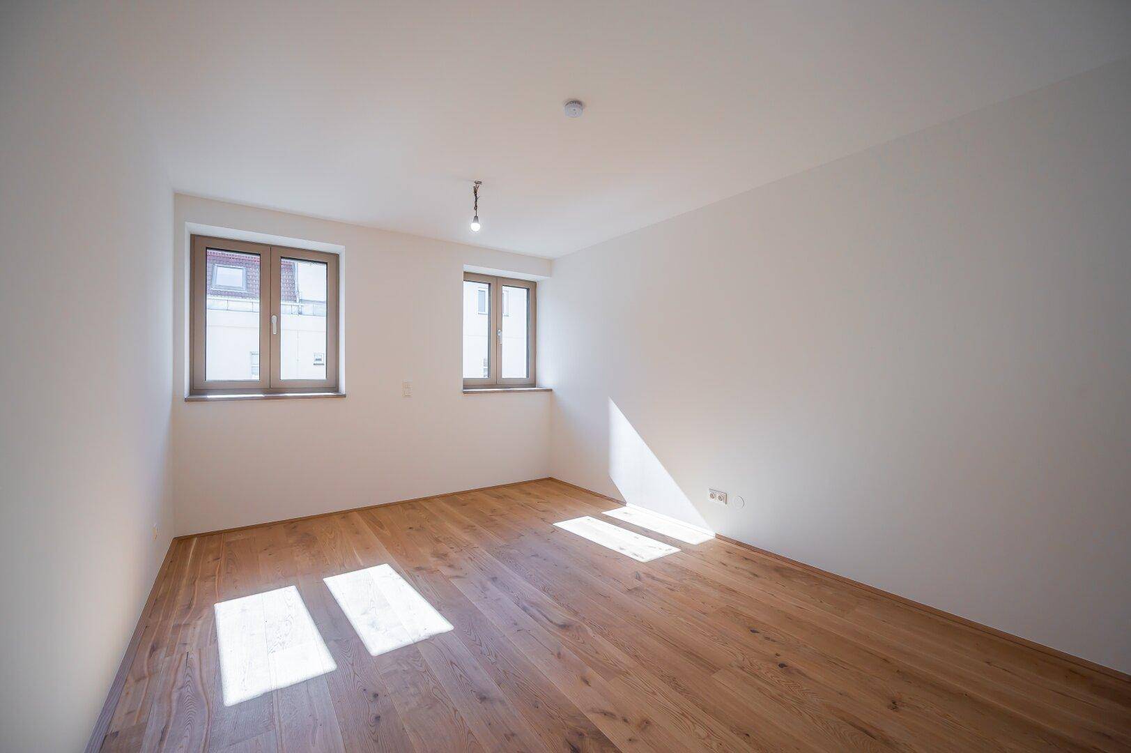 Helles Schlafzimmer mit Holzboden und zwei Fenstern für viel natürliches Tageslicht.