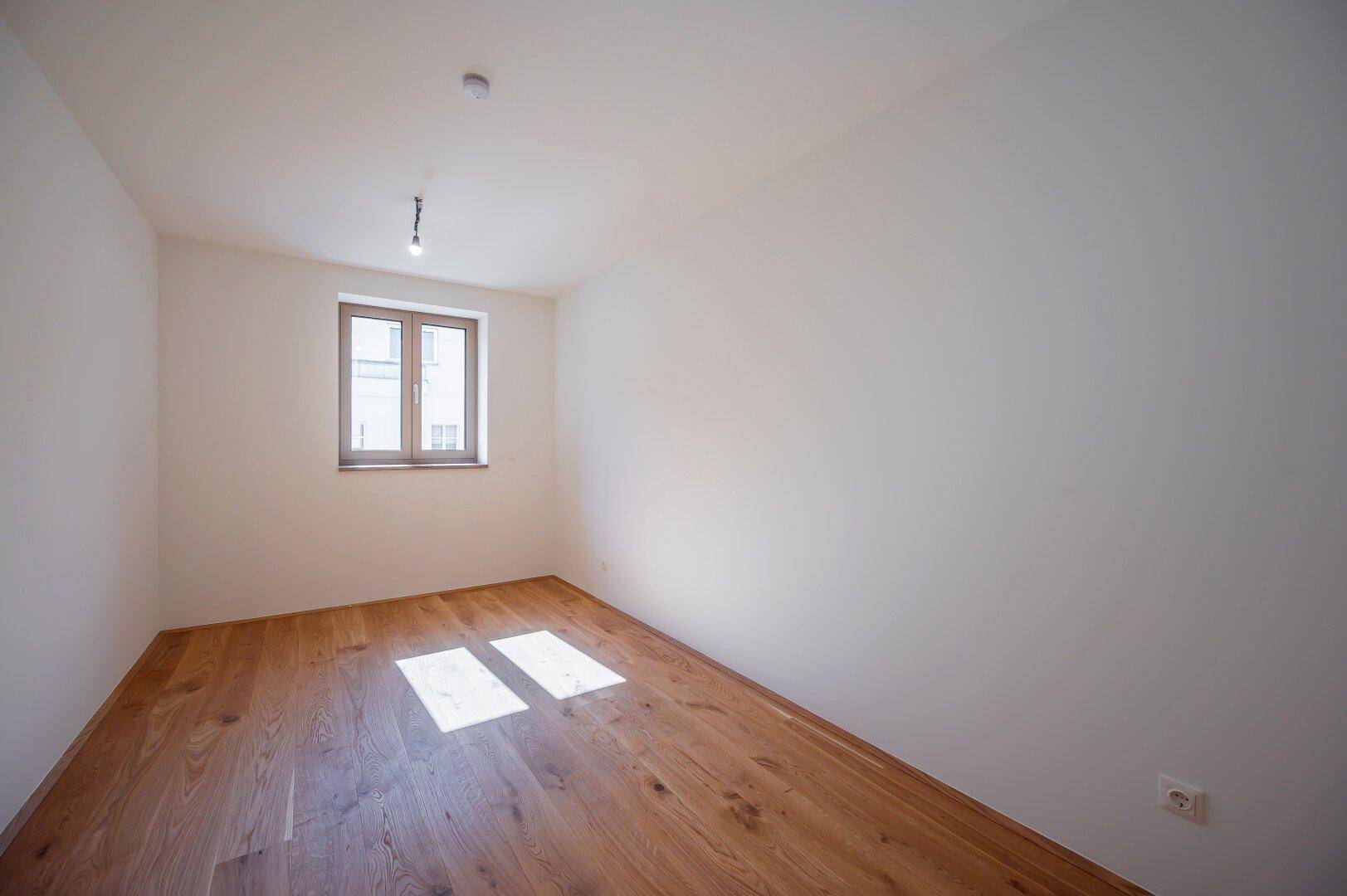 Geräumiges Schlafzimmer mit Holzboden und einem großen Fenster für angenehme Helligkeit.