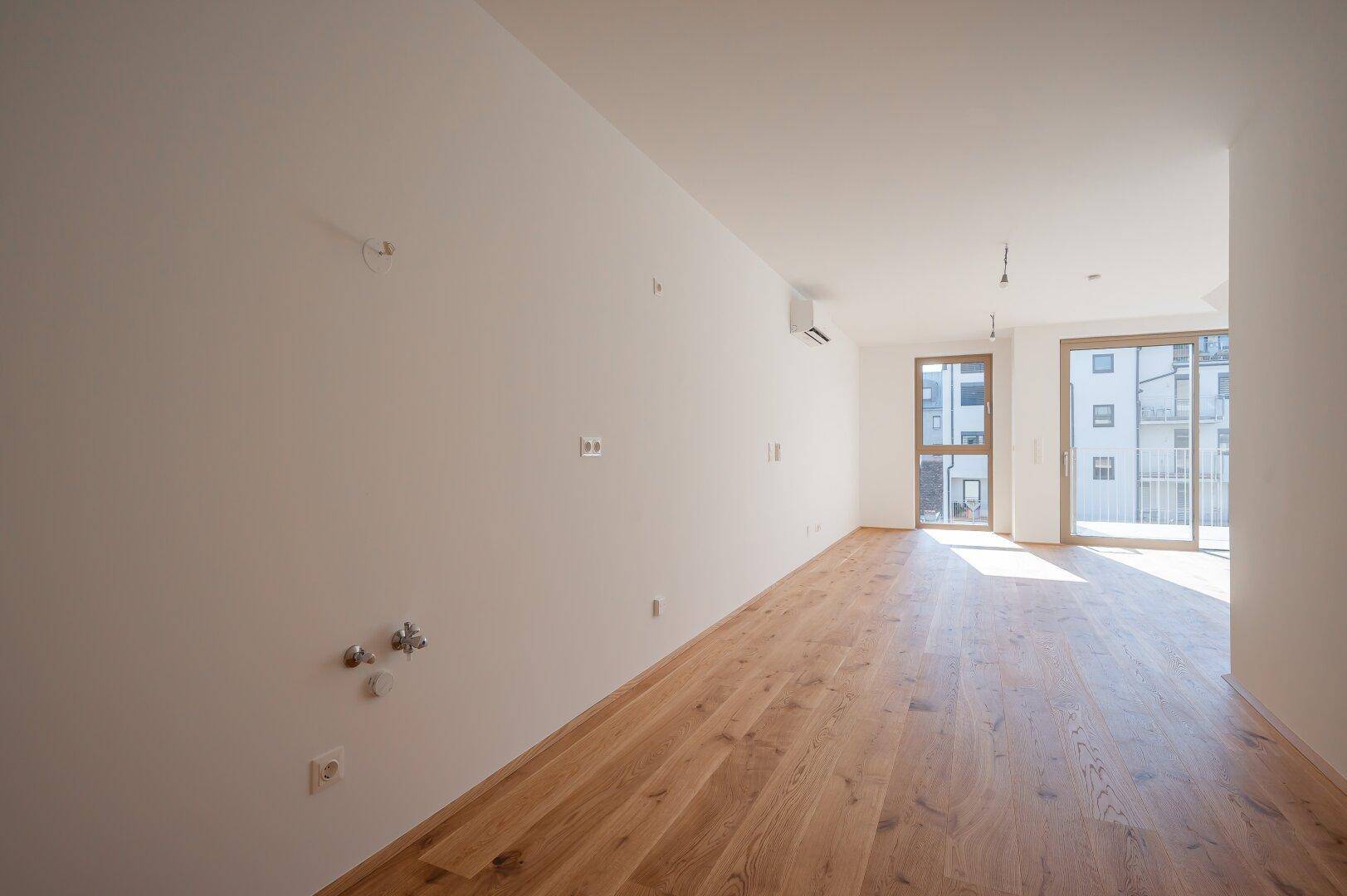 Lichtdurchfluteter Raum mit Holzboden, großen Fenstern und einer modernen Klimaanlage.