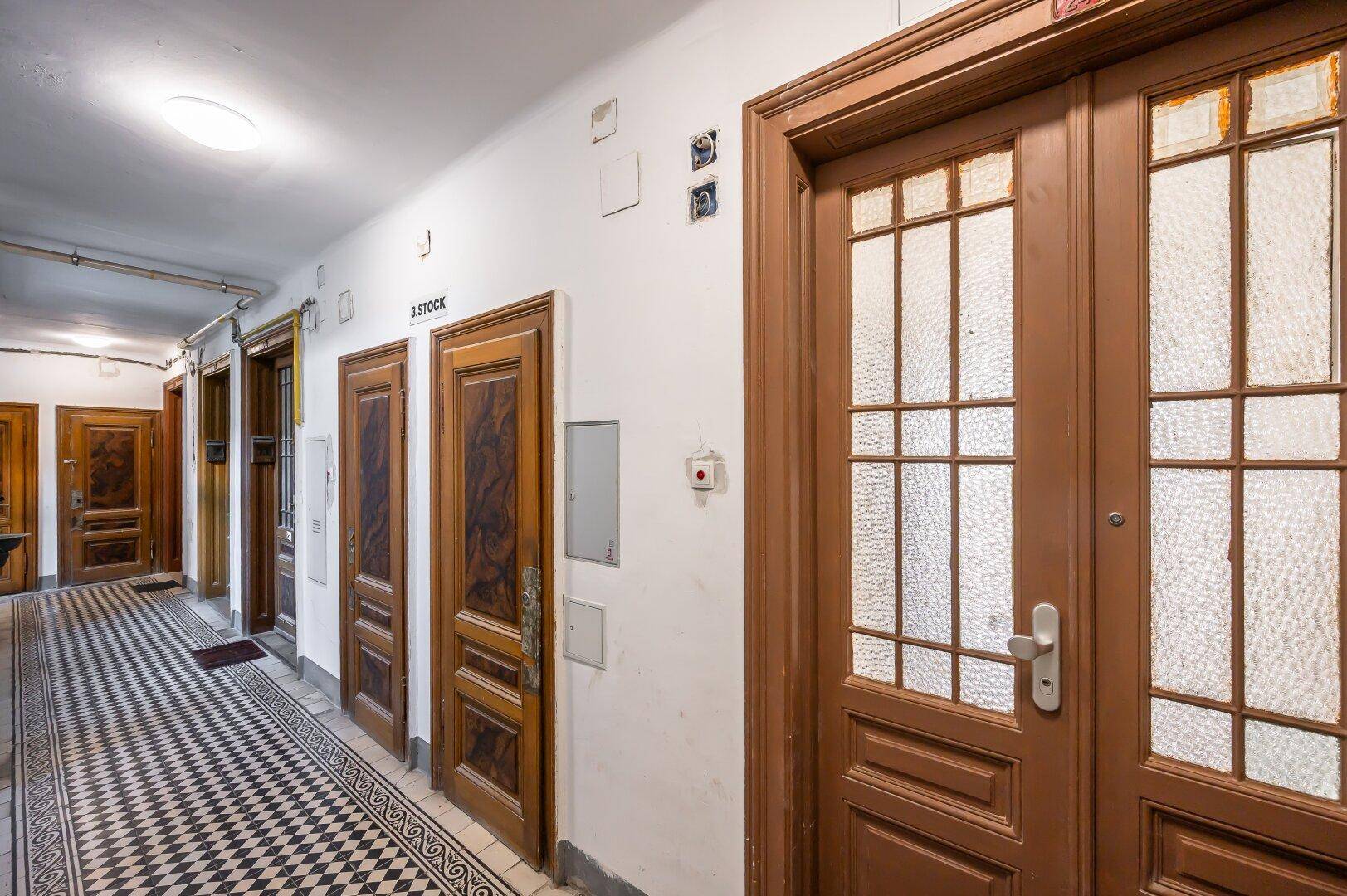Gemeinschaftsflur in einem Altbau mit mehreren Holztüren und gemustertem Fliesenboden.