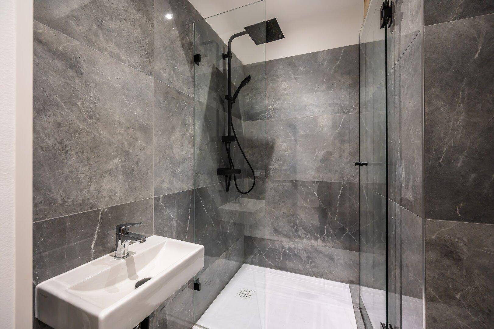 Modernes Badezimmer mit grauen Marmorfliesen, wandmontiertem Waschbecken und begehbarer Regendusche.