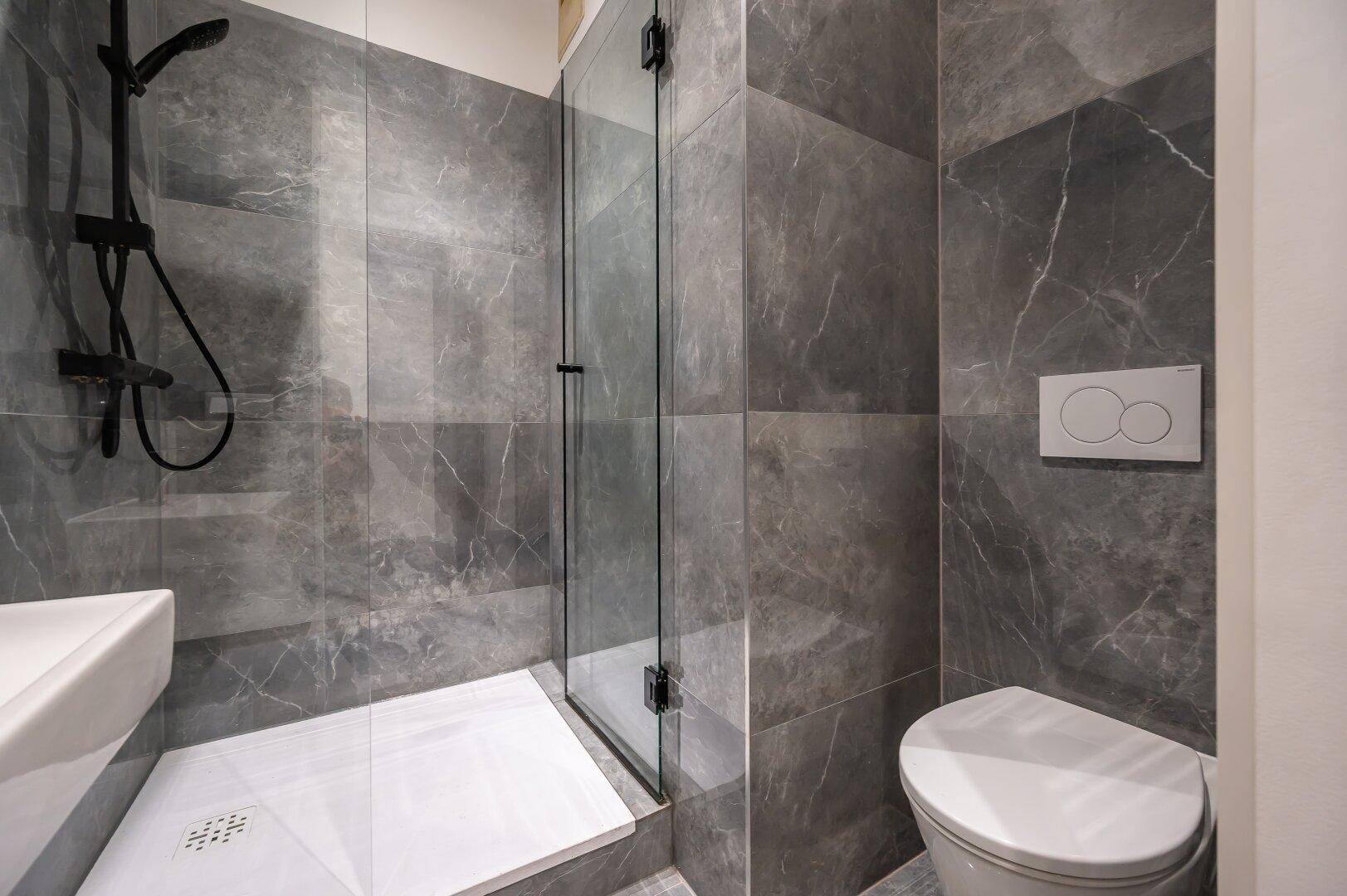 Modernes Badezimmer mit grauen Marmorfliesen, wandmontierter Toilette und begehbarer Dusche.