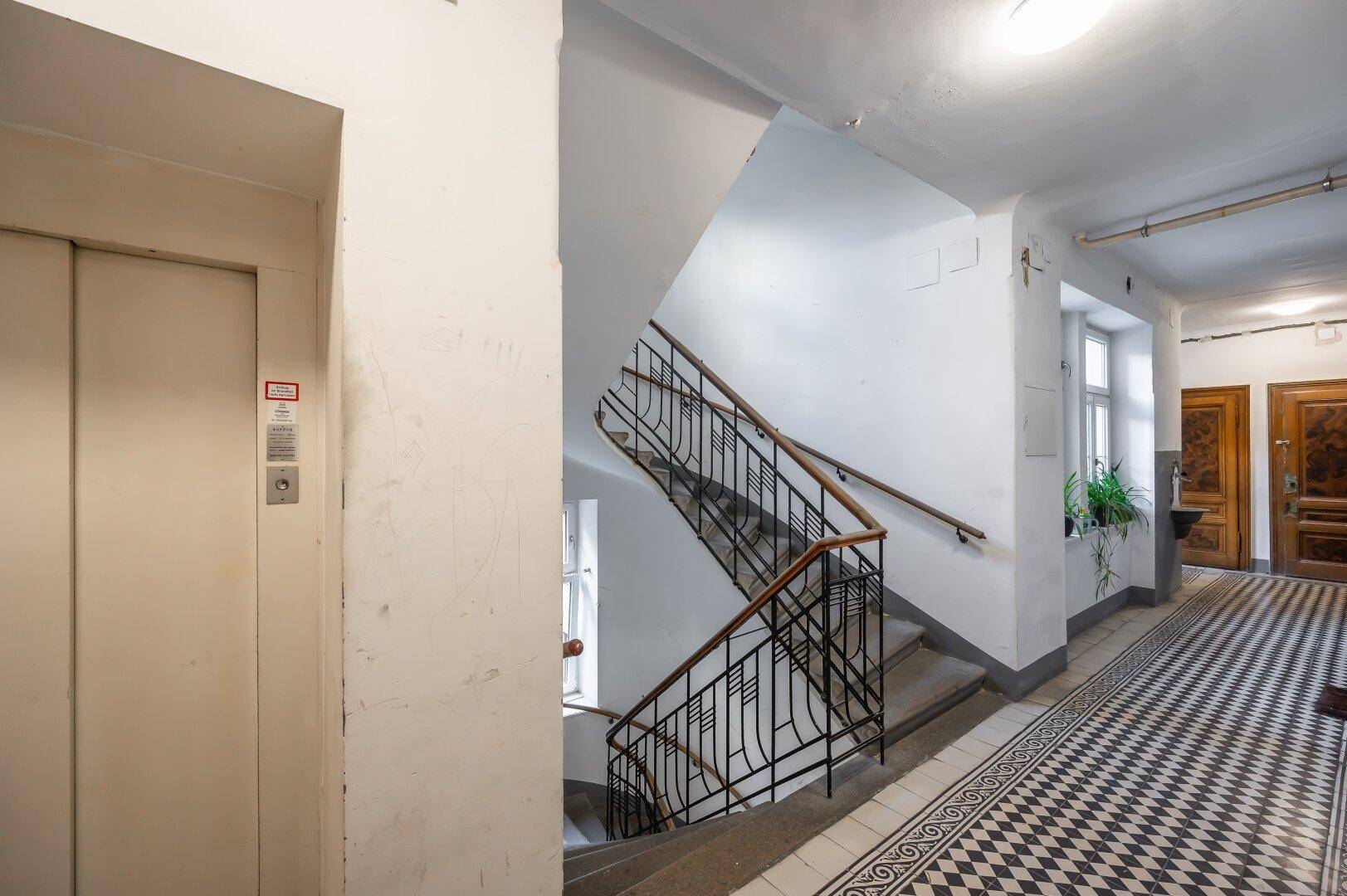 Gemeinschaftsflur in einem Altbau mit Aufzug, Treppenhaus und gemustertem Fliesenboden.