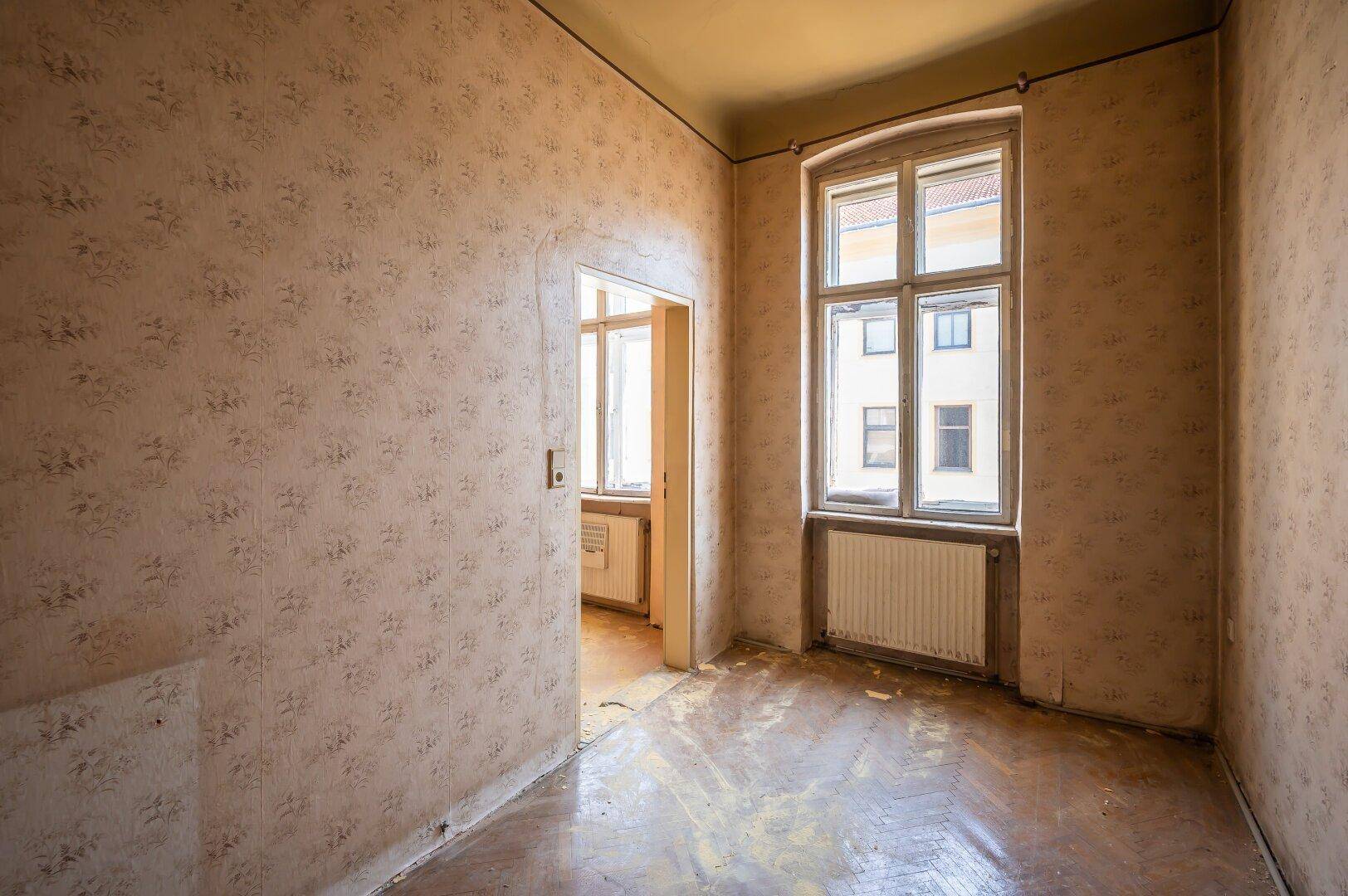 Leerer Raum mit einem Fenster und abgenutztem Boden, der auf eine umfassende Modernisierung wartet.