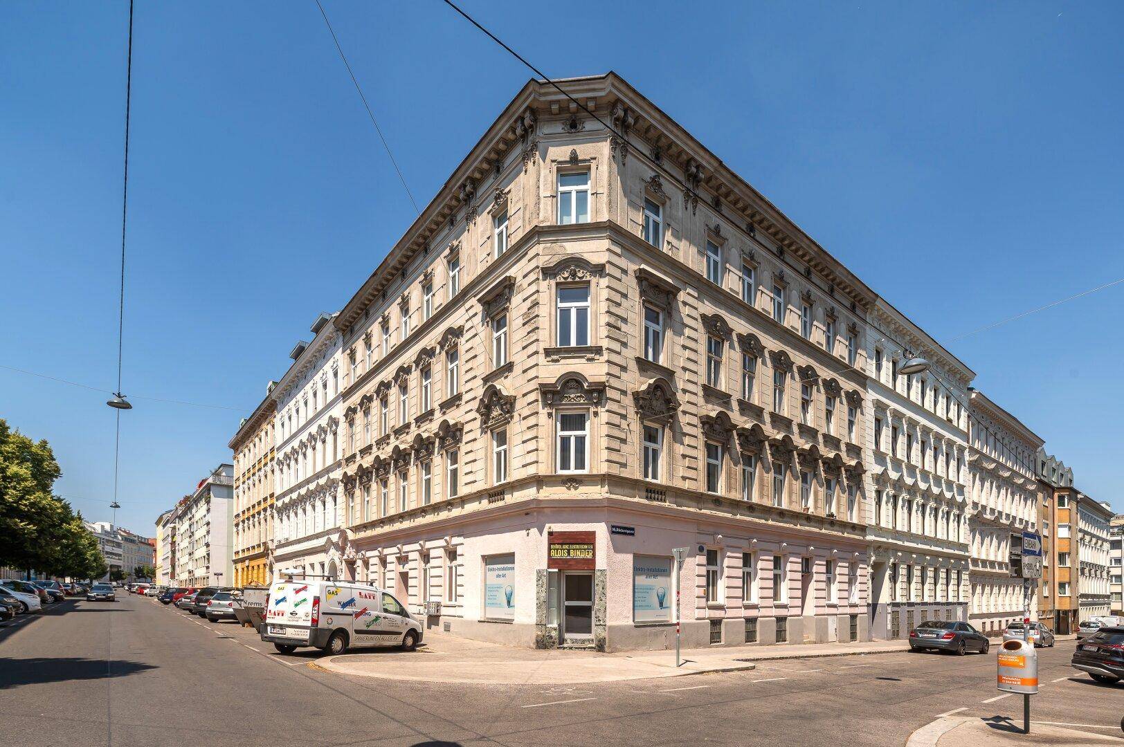 Historisches Eckgebäude mit eleganter Fassade an einer sonnigen Stadtkreuzung.