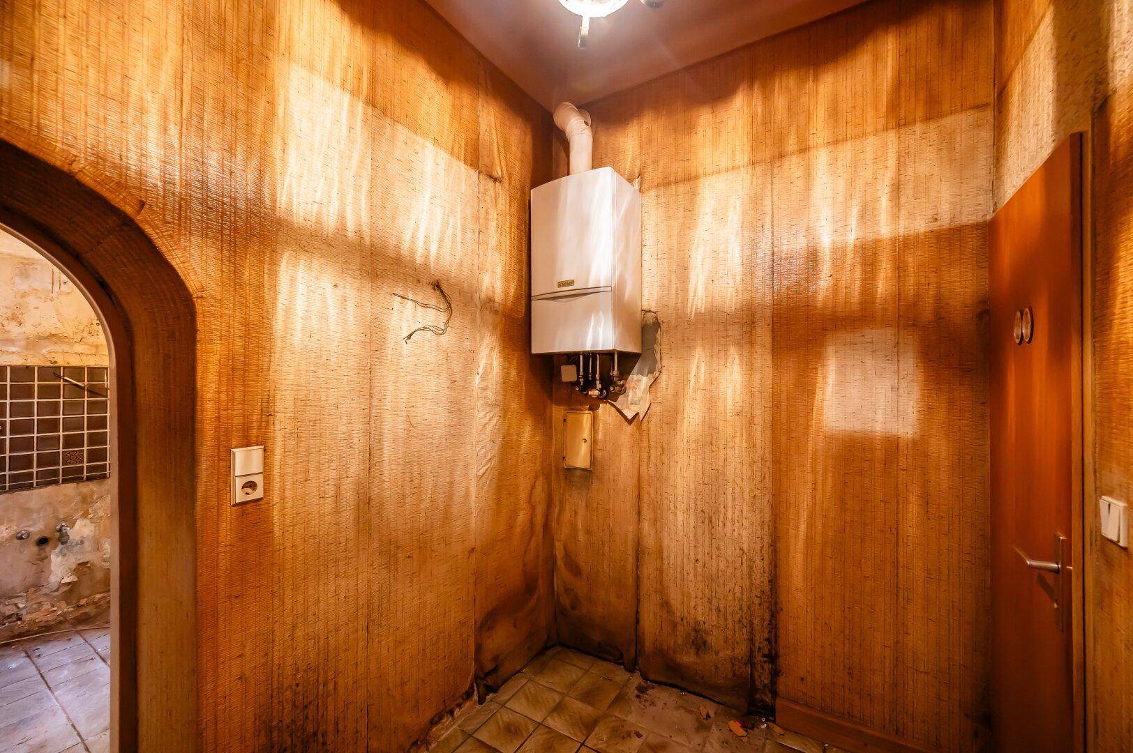 Kleiner Hauswirtschaftsraum mit einem Gasboiler an der Wand und abgenutzter Tapete.