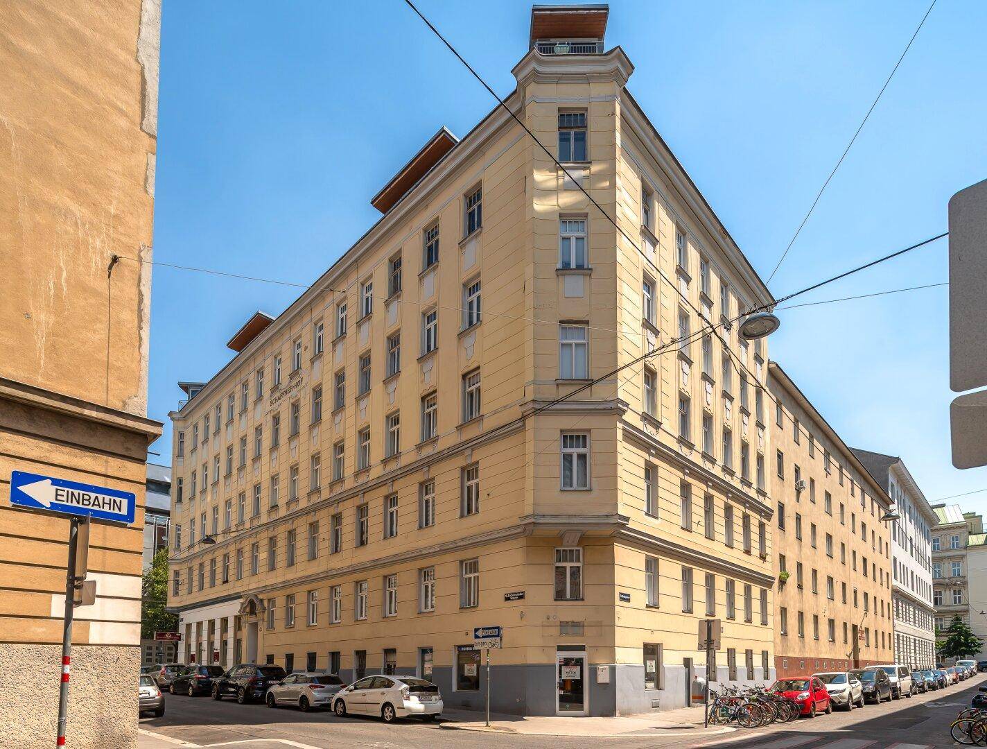 Eckgebäude mit klassischer Architektur und vielen Fenstern in einer städtischen Umgebung.