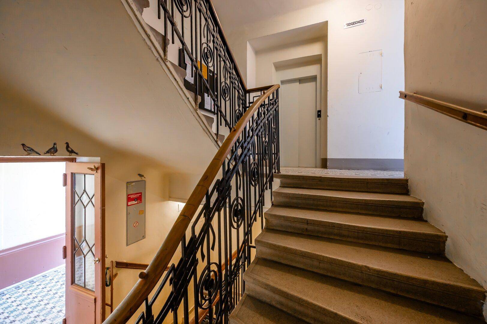 Treppenhaus mit Steinstufen und schmiedeeisernem Geländer, inklusive Zugang zum Aufzug.