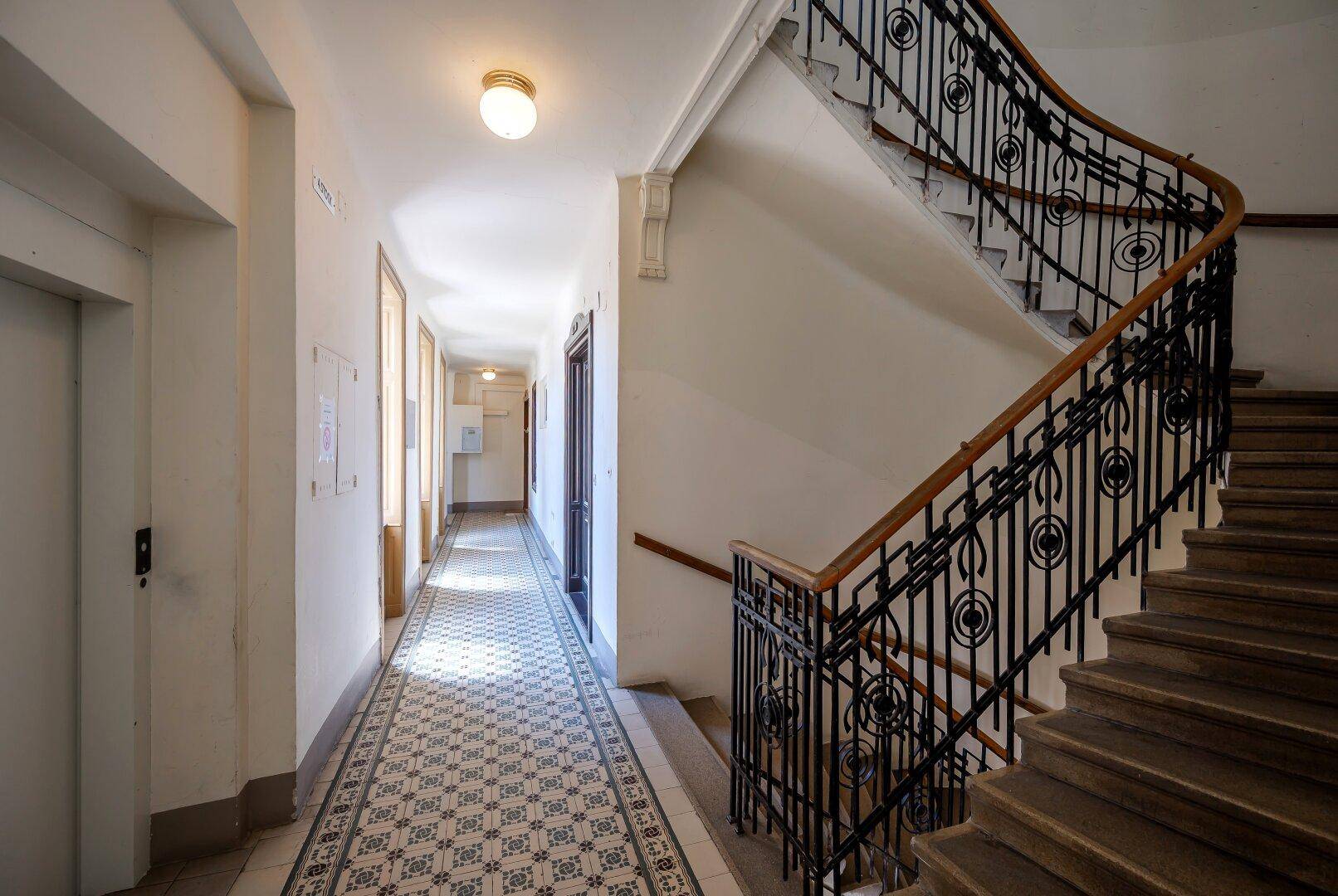 Elegantes Treppenhaus mit schmiedeeisernem Geländer und gemustertem Fliesenboden in einem Altbau.