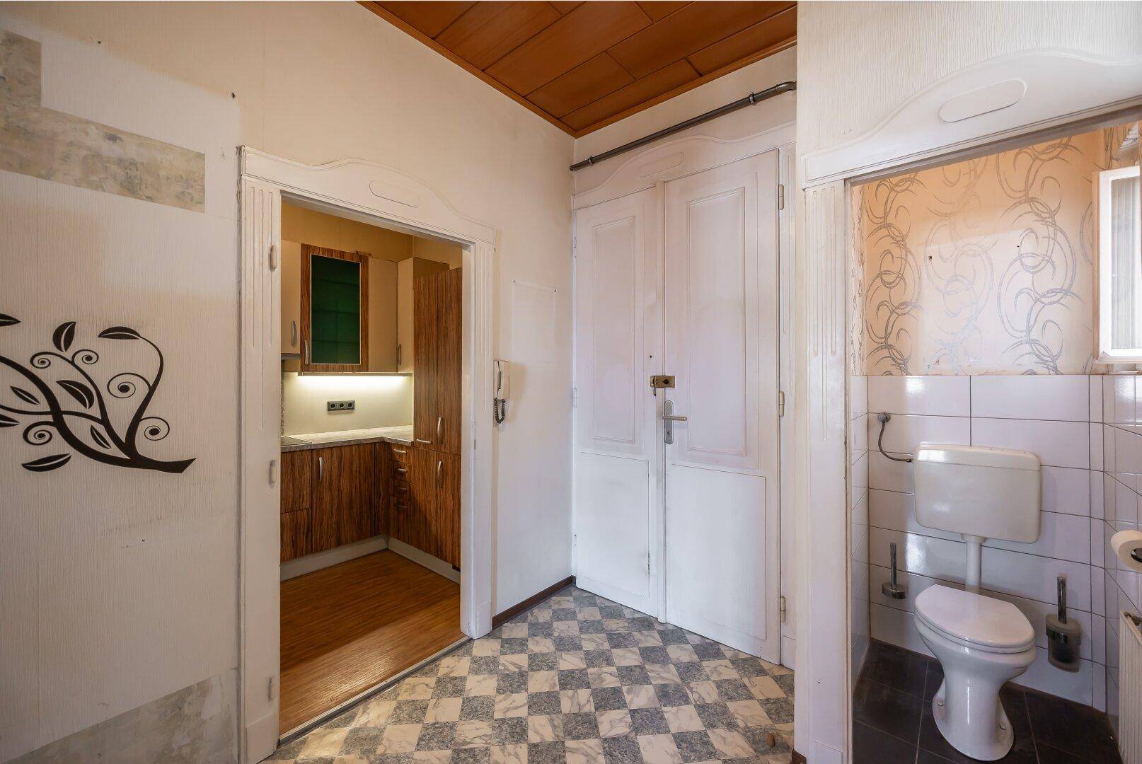 Flur mit kariertem Fliesenboden, der zu einer Küche und einem separaten WC führt.