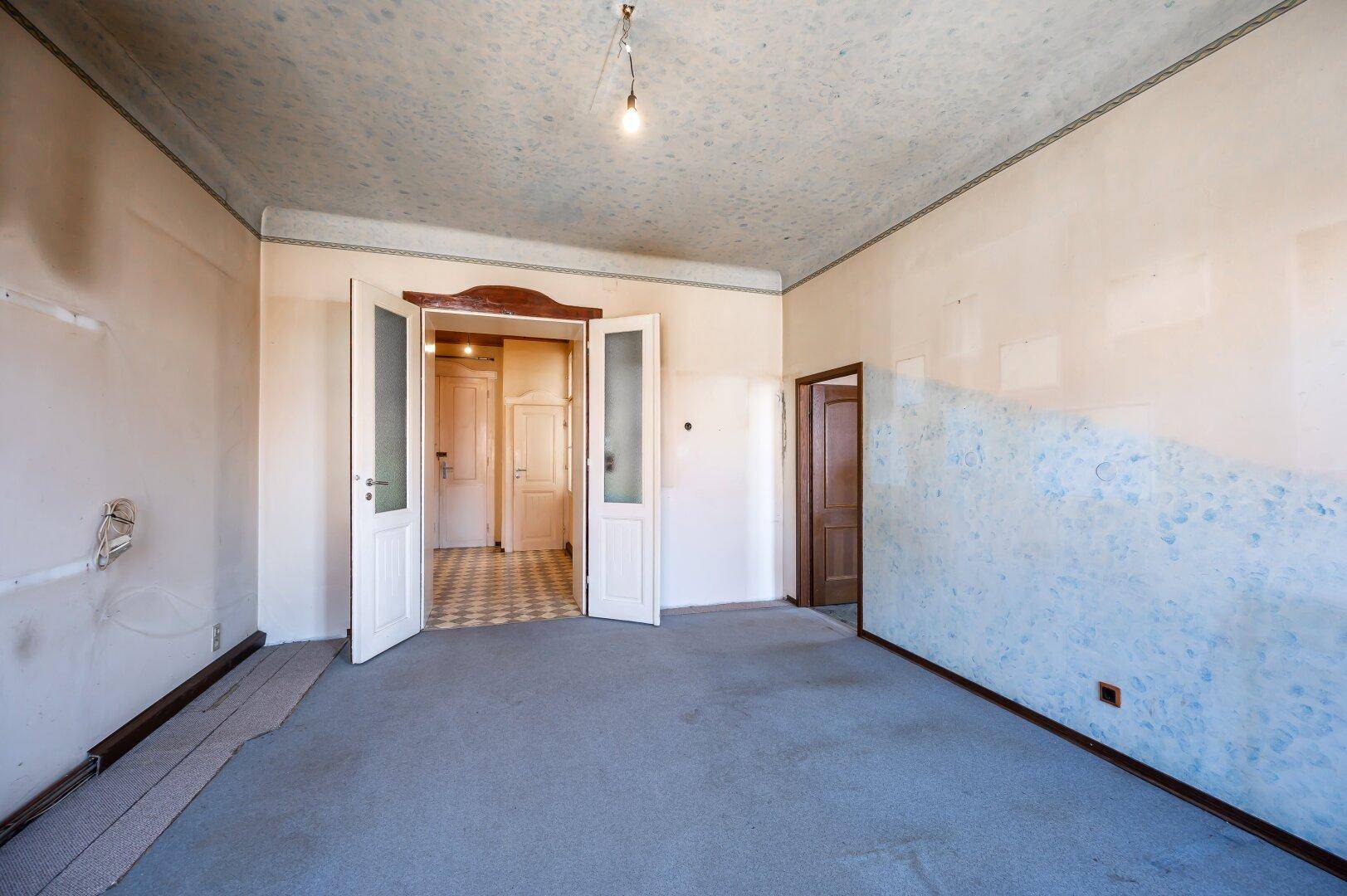 Geräumiges, unmöbliertes Zimmer mit Teppichboden und Doppeltüren, bereit zur Renovierung.
