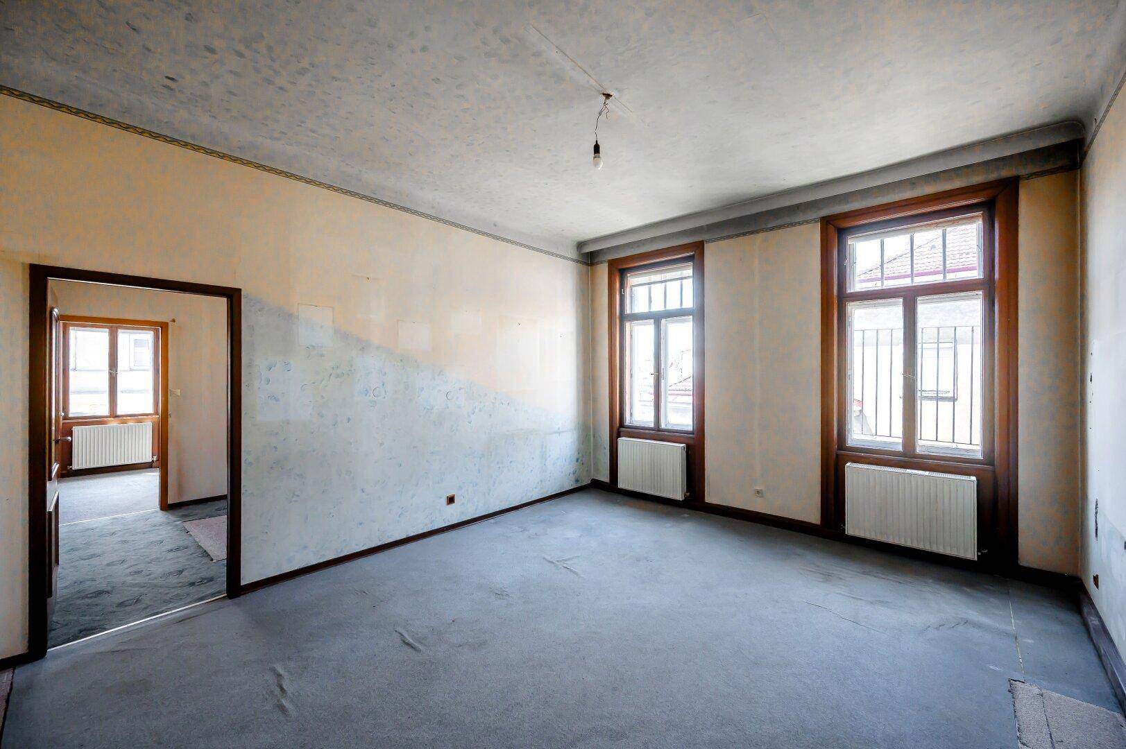 Helles, unmöbliertes Zimmer mit Teppichboden und zwei großen Fenstern, ideal für eine Neugestaltung.