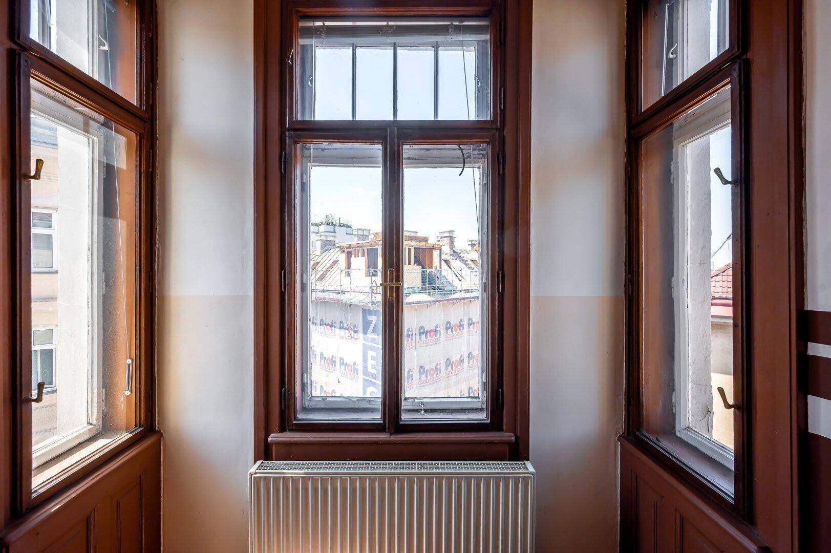 Detailansicht eines Holzfensters mit Blick auf die Dächer der umliegenden Gebäude.