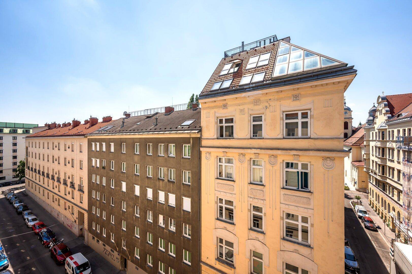 Historisches Gebäude mit Mansarddach und umliegenden Gebäuden in einer städtischen Umgebung.
