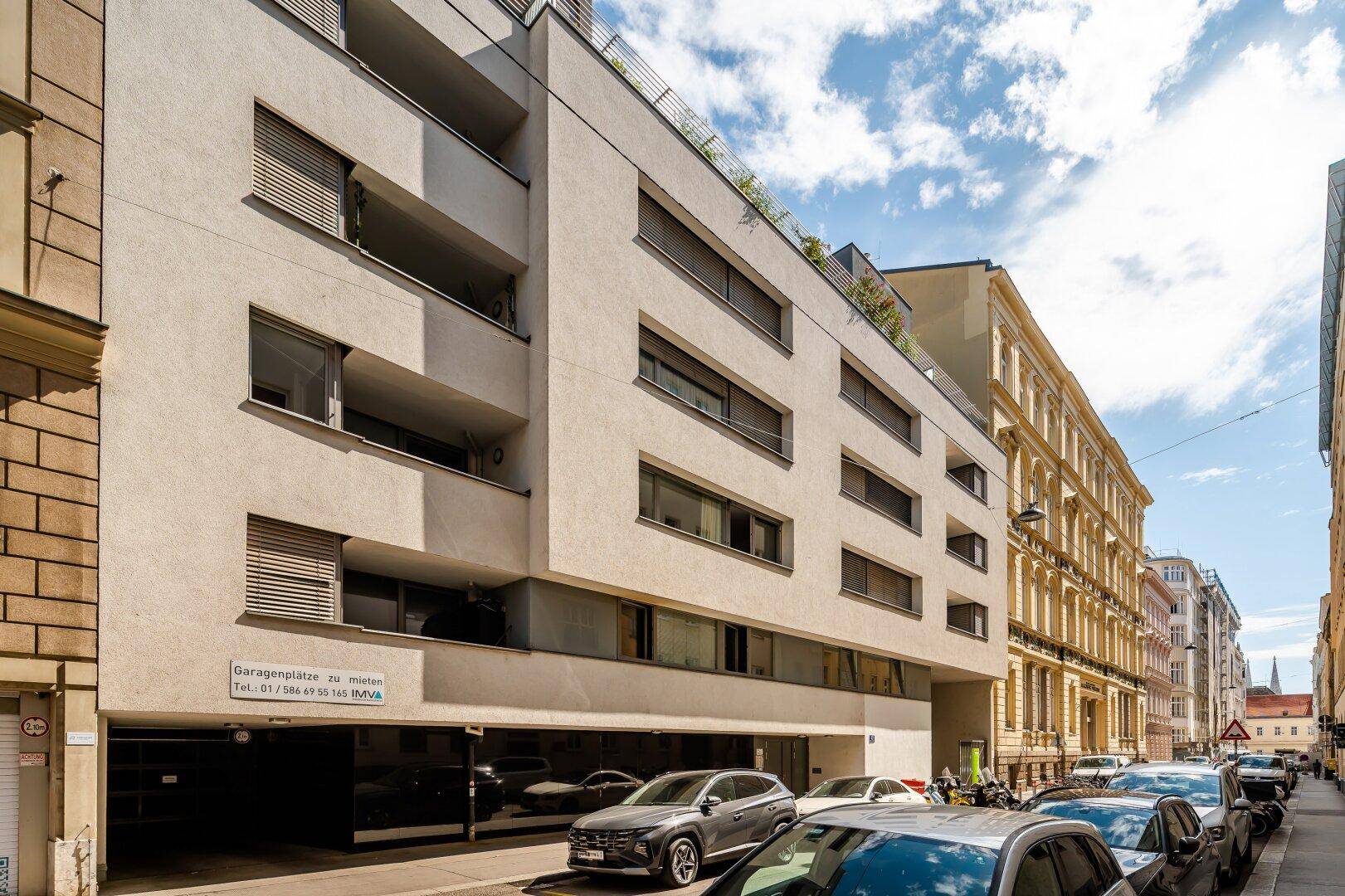 Moderne Wohngebäude-Fassade mit Garageneinfahrt und parkenden Autos an der Straße.