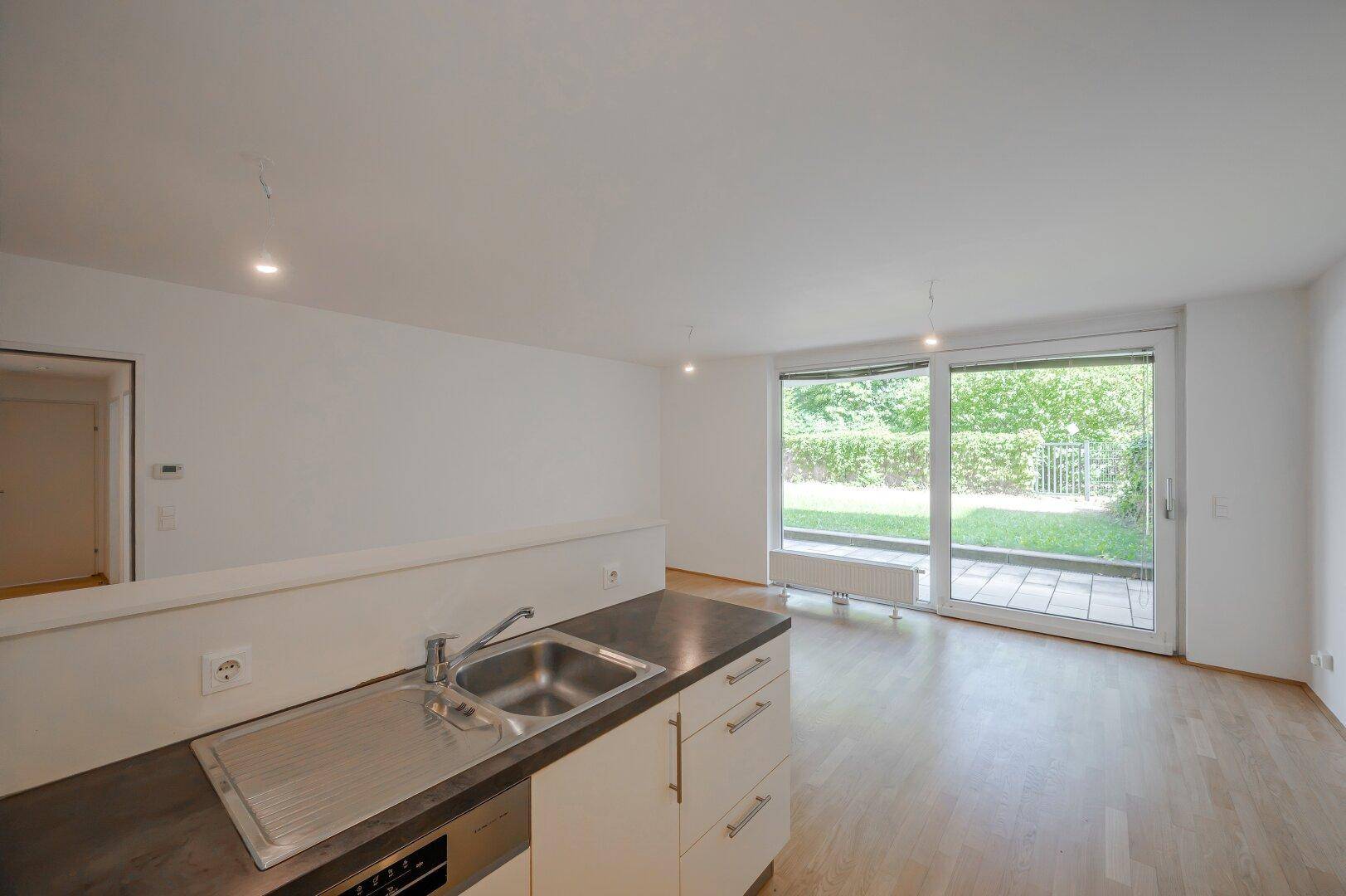 Moderne Küchenzeile mit Spüle und Arbeitsplatte, offen zum Wohnbereich mit Gartenblick.