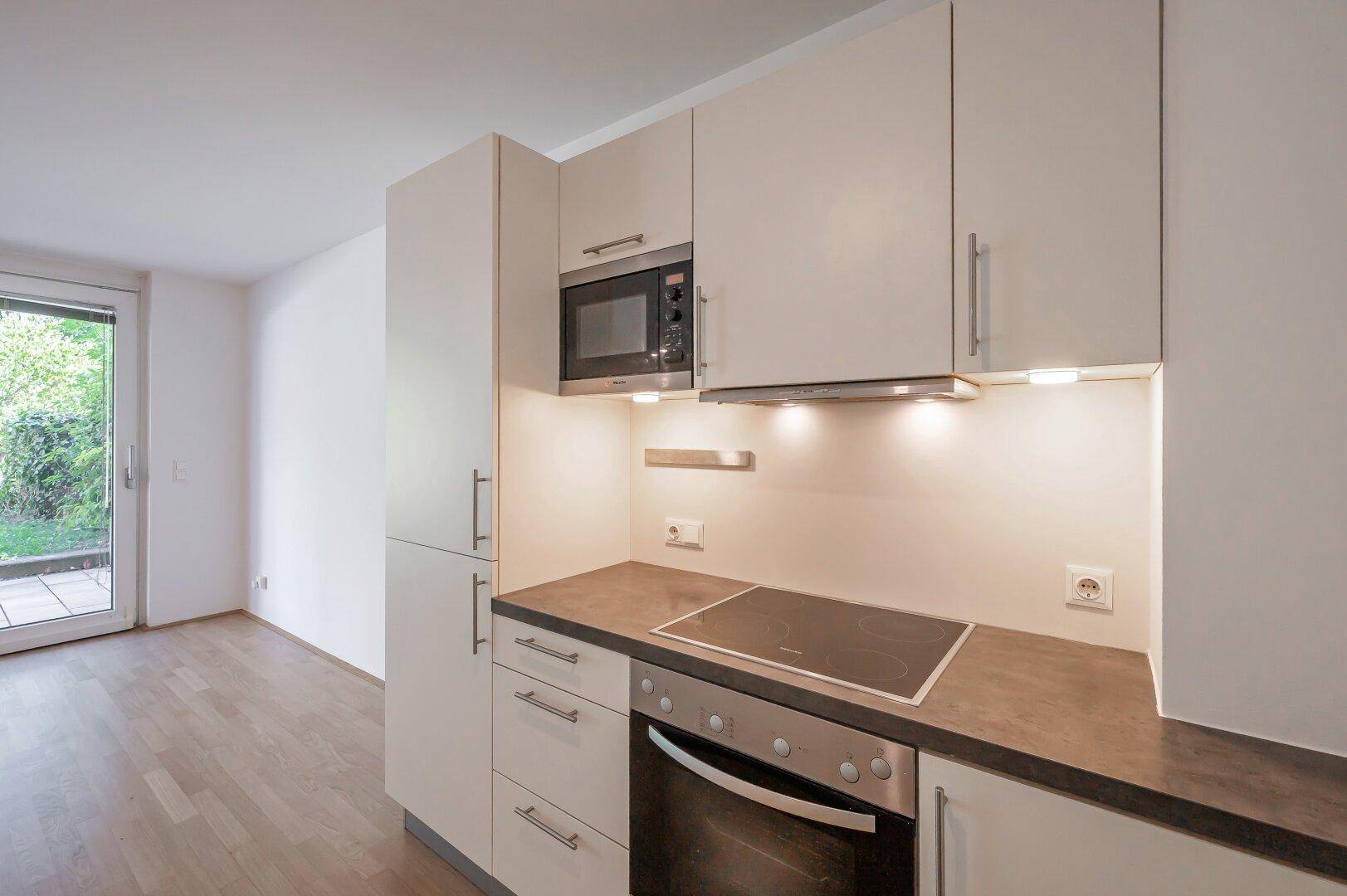 Kompakte Einbauküche mit Mikrowelle, Kochfeld und Backofen, ideal für offene Wohnkonzepte.