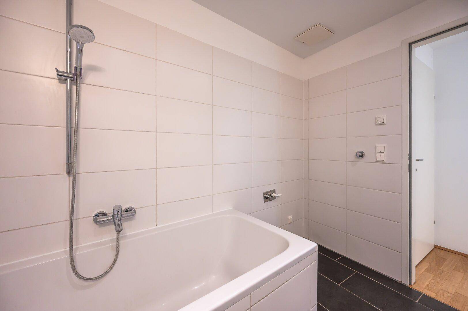 Modernes Badezimmer mit Badewanne, Duscharmatur und weißen Wandfliesen.