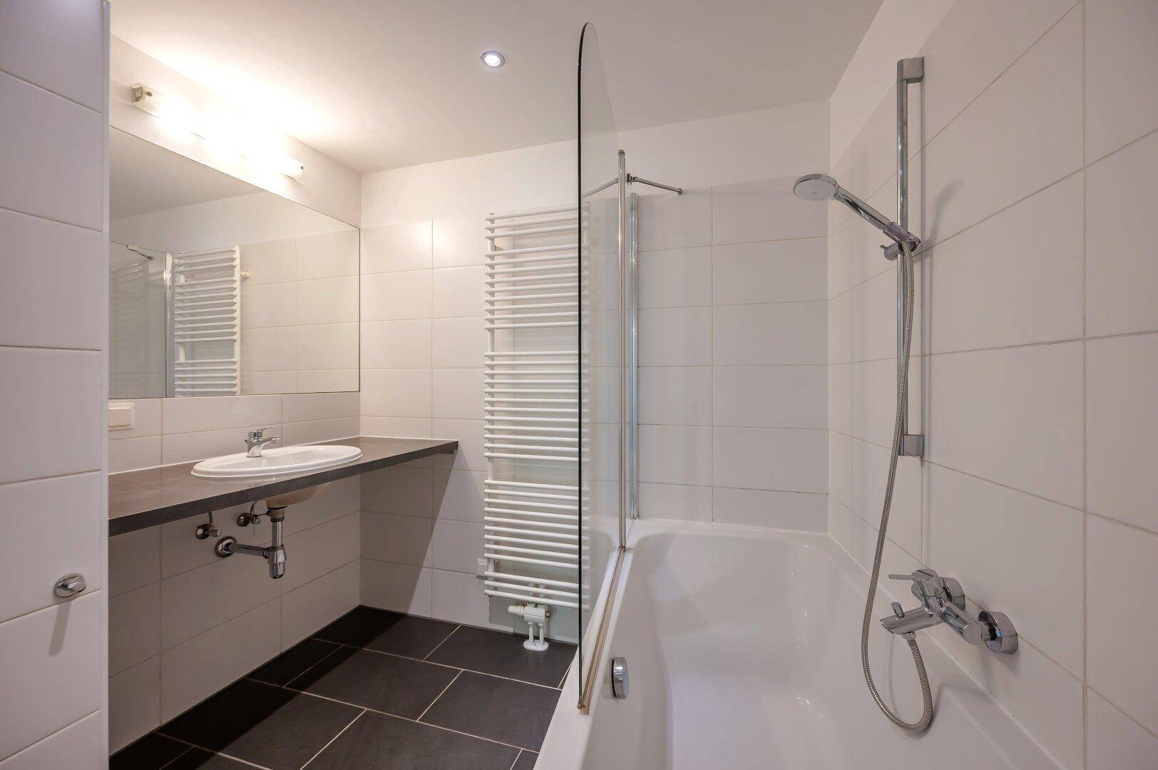 Helles Badezimmer mit Badewanne, Waschbecken, großem Spiegel und beheiztem Handtuchhalter.