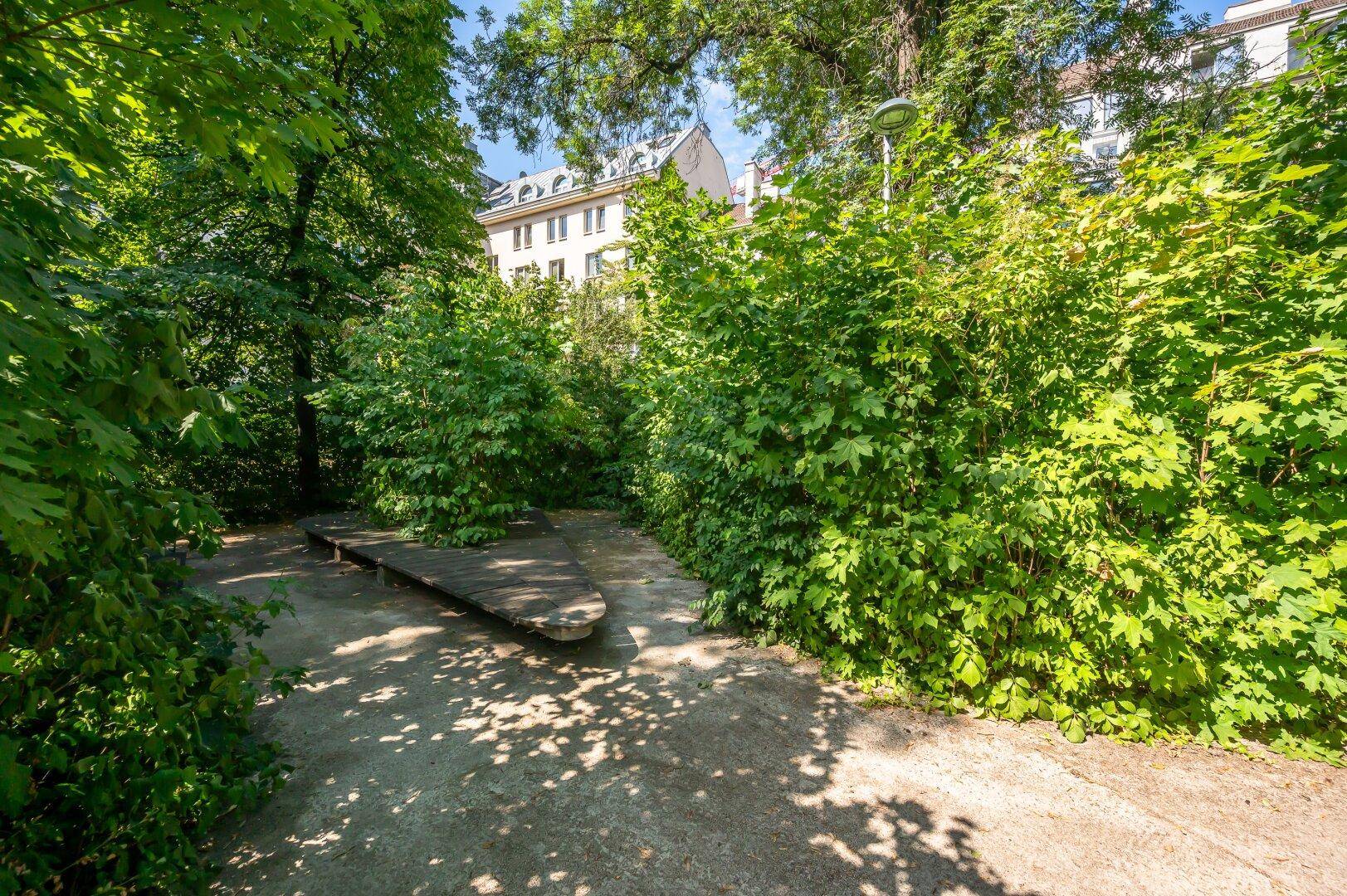 Ruhiger Gartenbereich mit üppiger Vegetation, Wegen und einer Holzbank zum Entspannen.