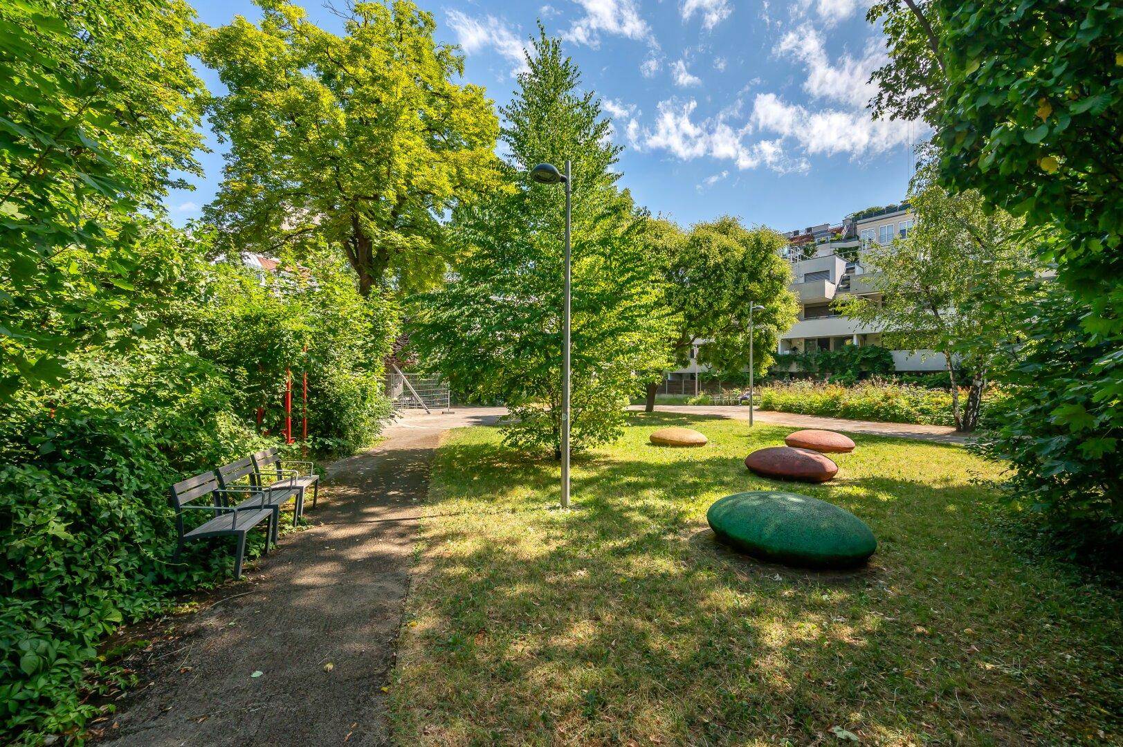 Öffentlicher Parkbereich mit Bänken, Bäumen und dekorativen Steinen in einer Grünanlage.